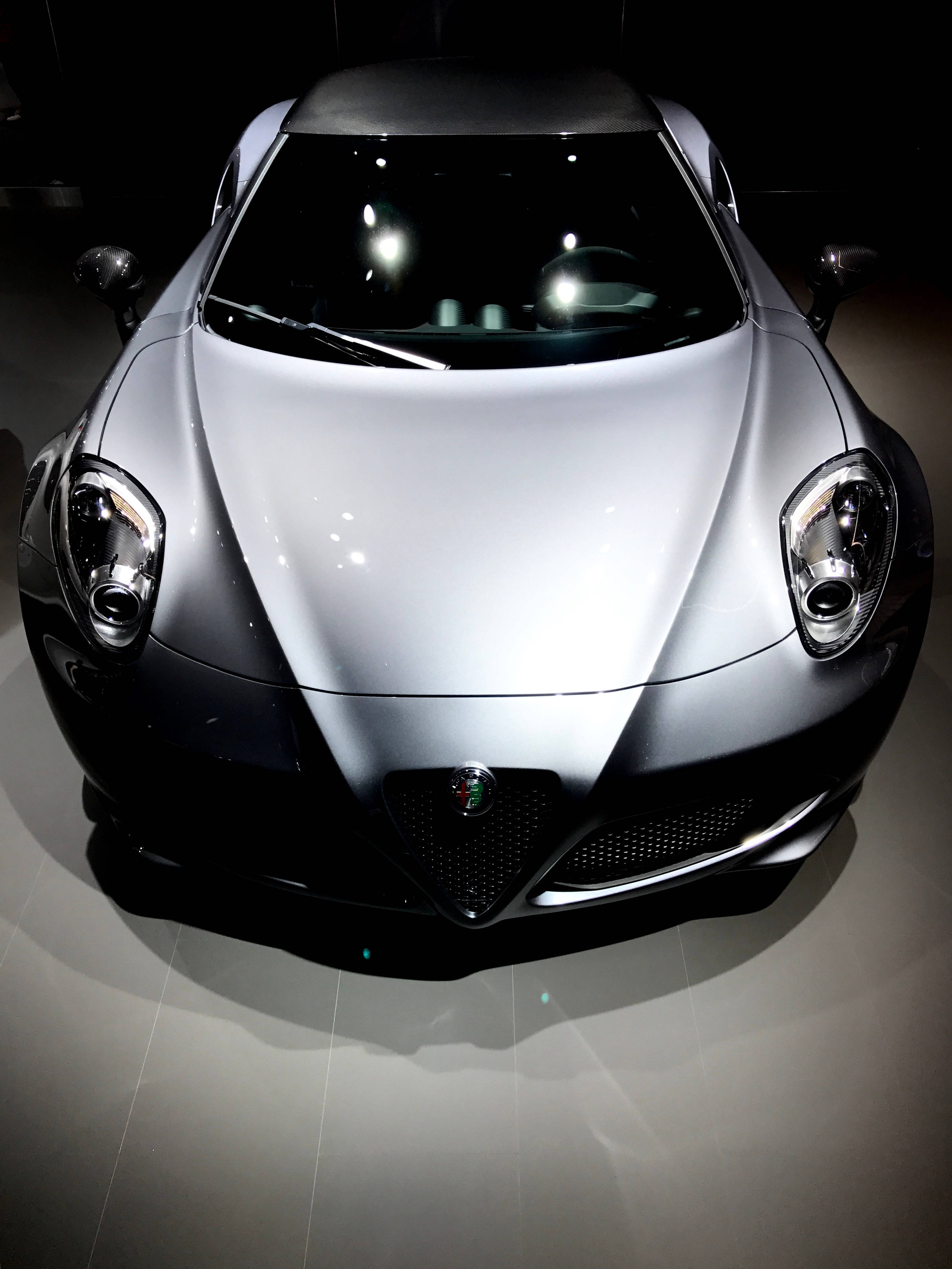 愛快羅密歐 桌布 壁紙 — 一輛時尚的銀色阿爾法羅密歐跑車在黑暗的展廳中，在聚光燈下閃閃發光，地板具有反射效果。