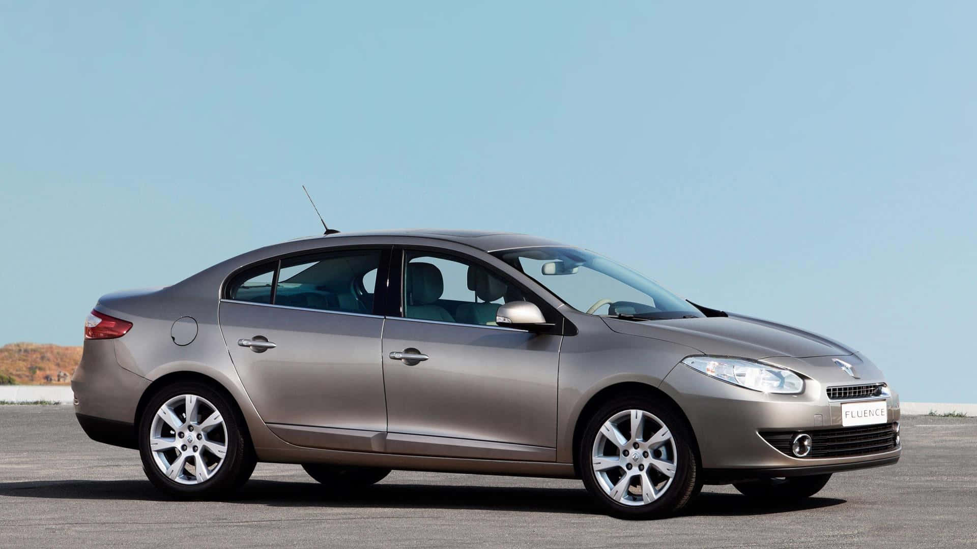 Renault Fluence 桌布 壁紙 — 一輛時尚的銀色雷諾 Fluence 轎車停放在開闊的鋪砌停車場上，天空清澈湛藍。