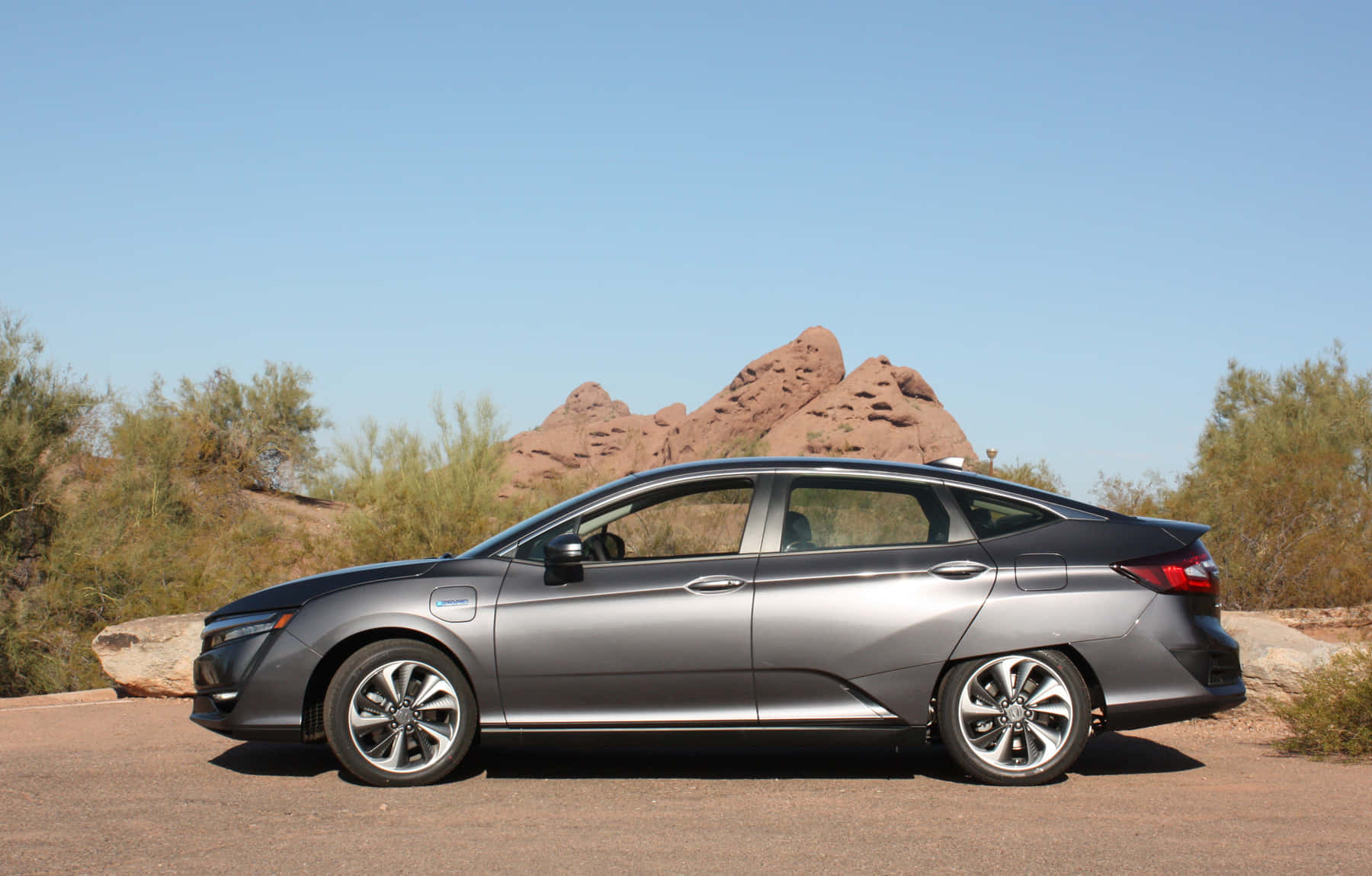 Honda Clarity 桌布 壁紙 — 一輛時尚的銀色電動車停在沙漠公路上，周圍有紅色岩層和綠色灌木，天空湛藍清澈。