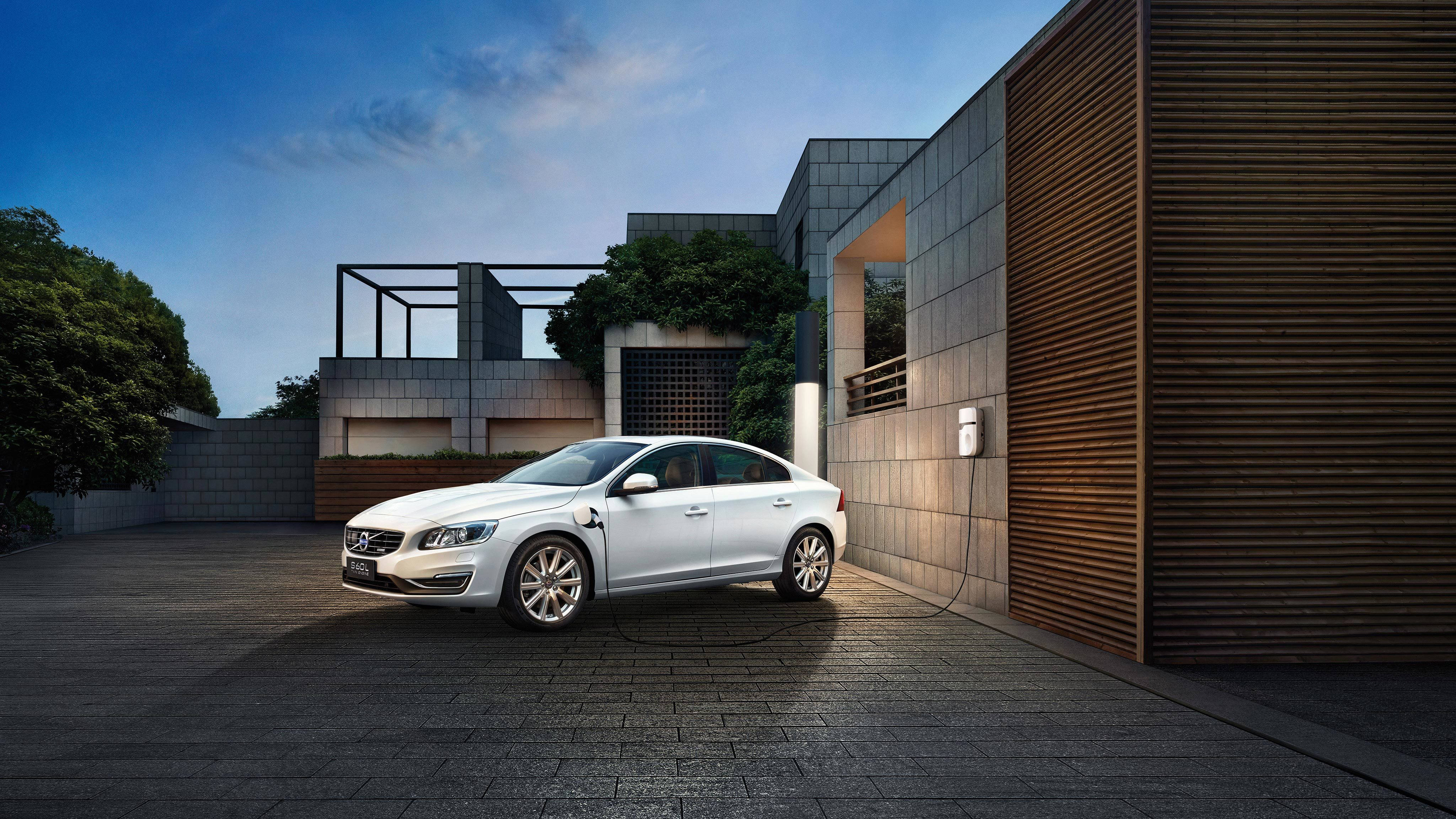 Volvo 桌布 壁紙 — 一輛時尚的銀色電動車在黃昏天空下，在一棟帶有木條牆的現代房屋旁充電。