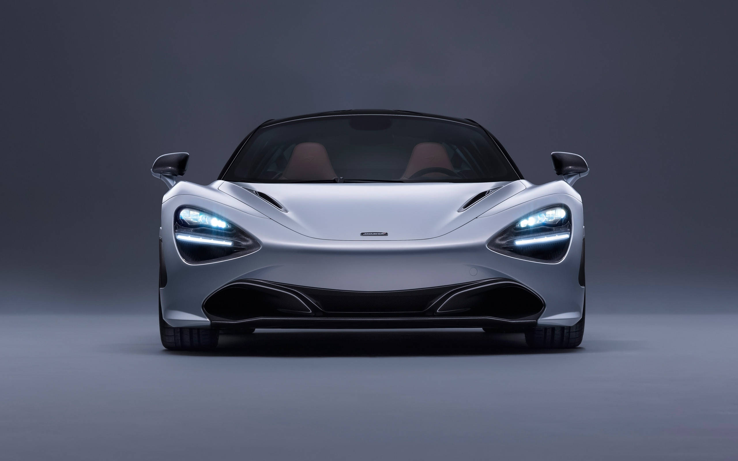 mclaren 720s 4K 桌布 壁紙 — 一輛時尚的銀色麥拉倫跑車，車頭燈發光，正面朝向深灰色工作室背景。