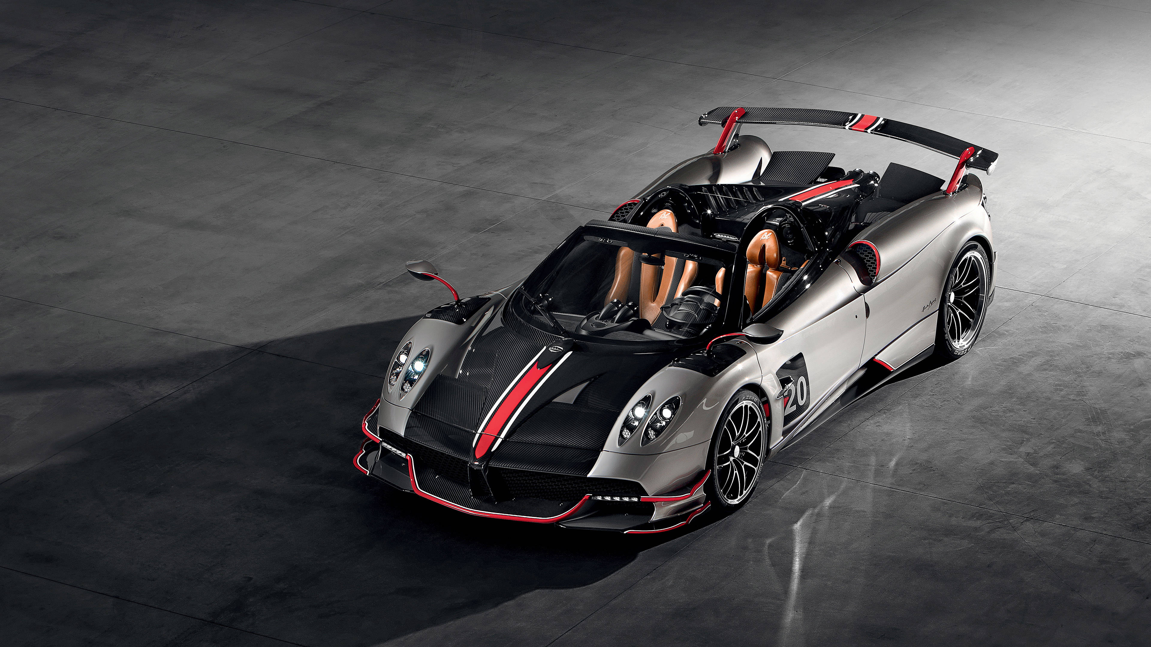 pagani iPhone 桌布 壁紙 — 一輛時尚的銀黑配色帕加尼 Huayra Roadster，帶有紅色點綴和賽車號碼20，停在工作室燈光下的深色混凝土地板上。