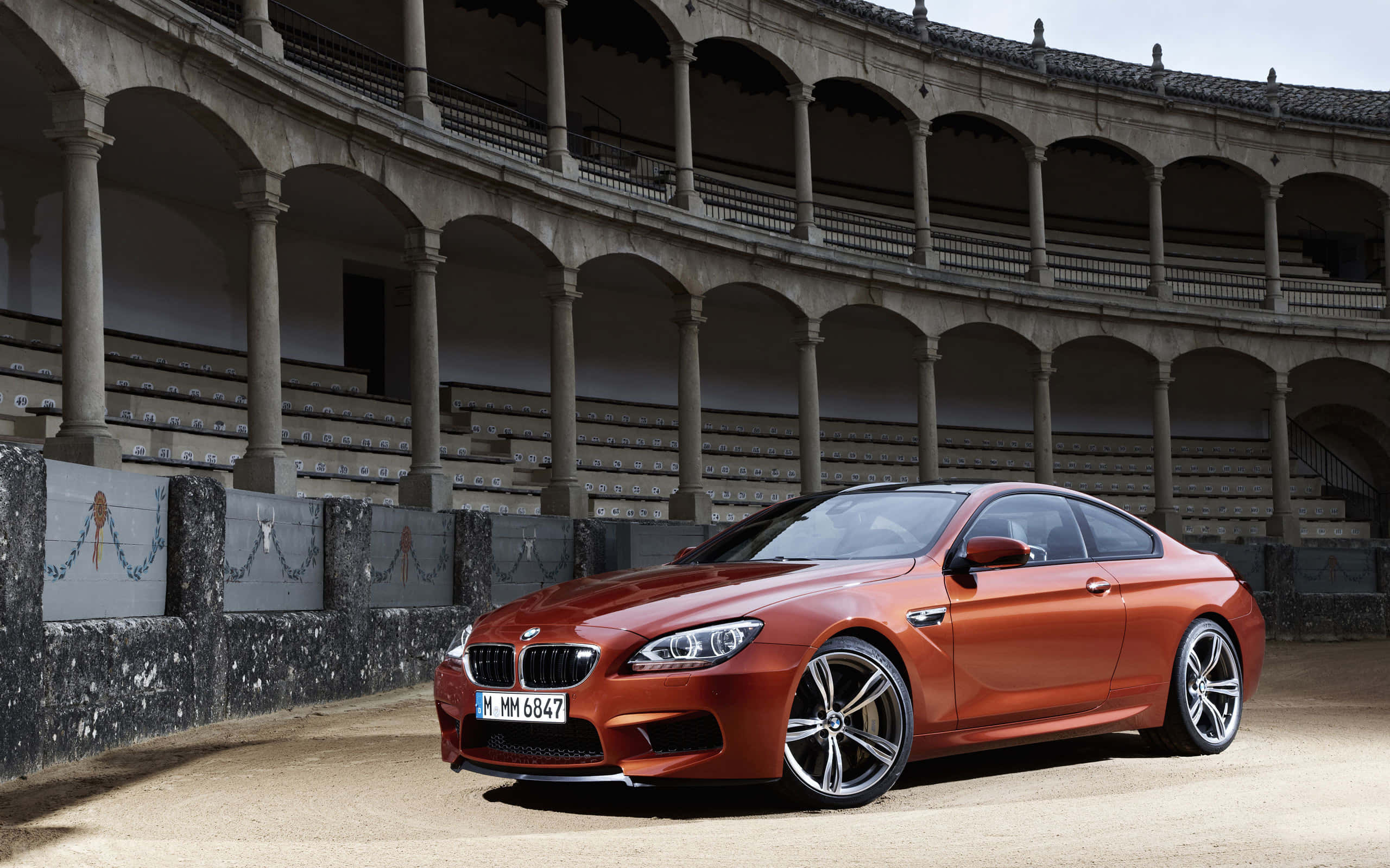 Bmw M6 桌布 壁紙 — 一輛時尚的銅色BMW M6雙門跑車停放在一個空無一人的歷史鬥牛場內，場內有石拱門和分層座位。