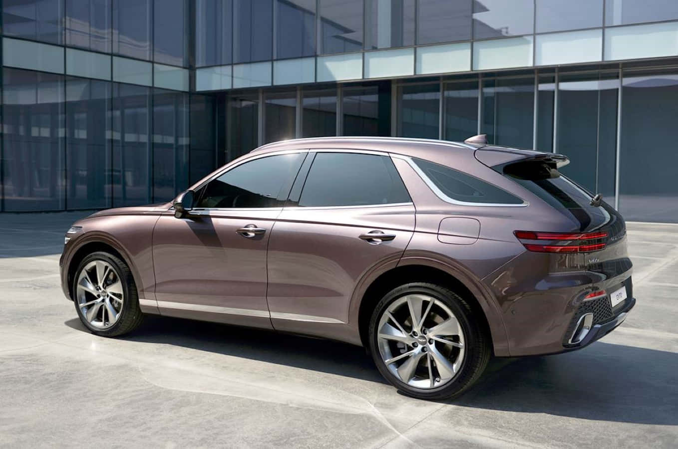 Genesis Gv70 桌布 壁紙 — 一輛時尚的銅色SUV在明亮的日光下停放在現代玻璃建築前。