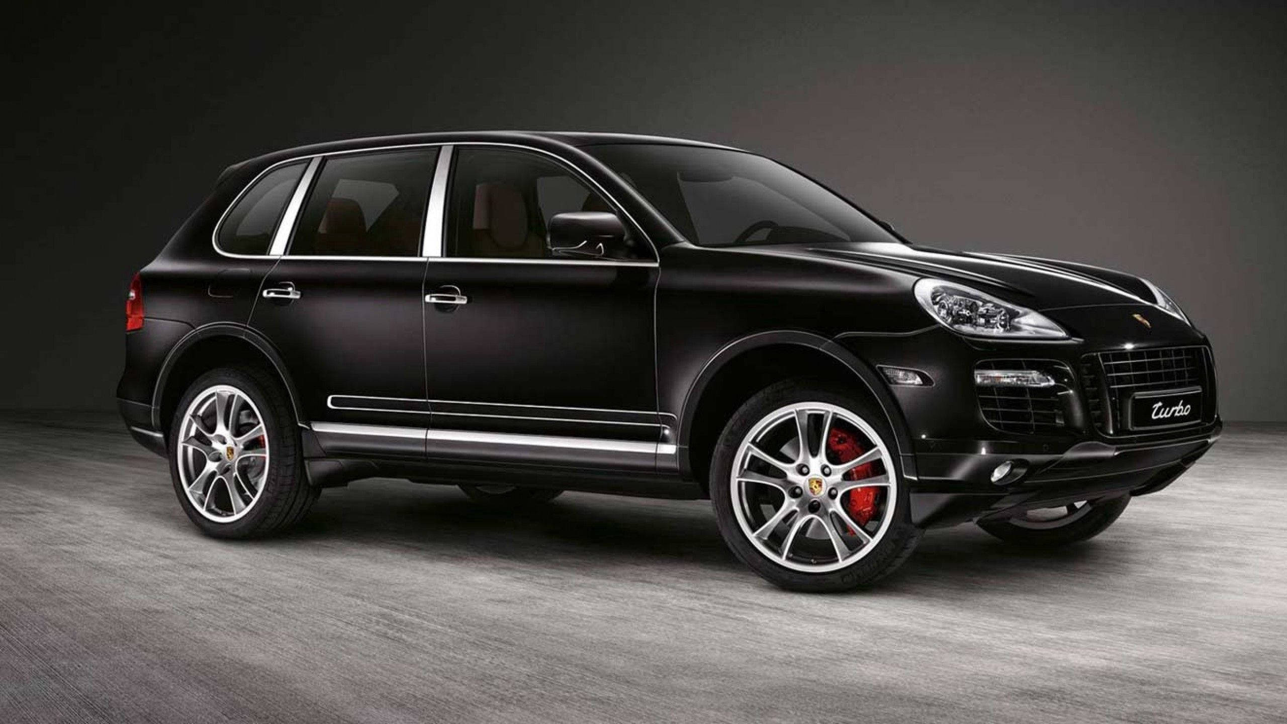 保時捷 桌布 壁紙 — 一輛時尚的霧面黑色保時捷凱宴 Turbo SUV，配備紅色制動卡鉗和銀色飾條，在簡約的攝影棚環境中蓄勢待發。