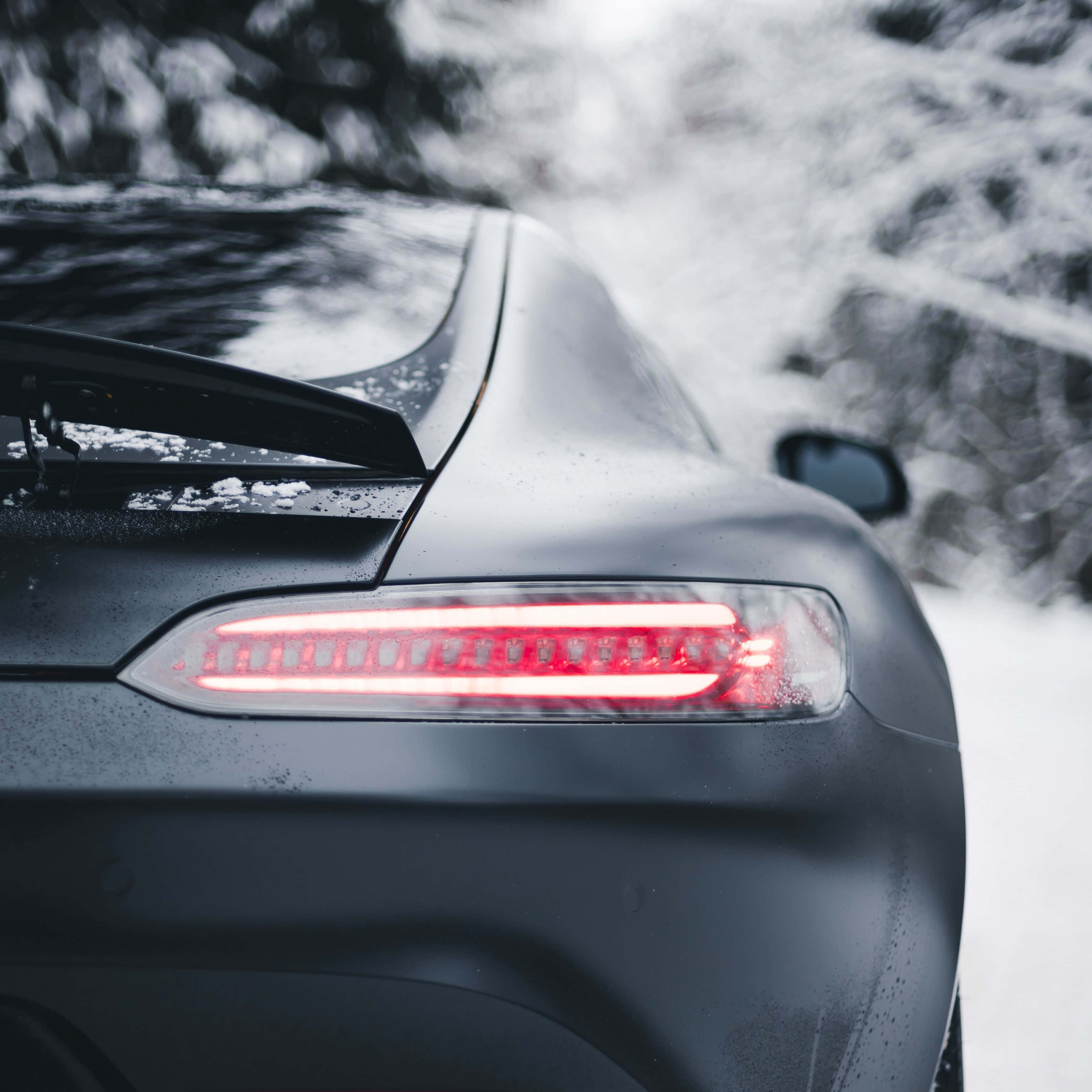 Mercedes 桌布 壁紙 — 一輛時尚的霧面黑色跑車，其發光的紅色尾燈劃過雪地森林背景。