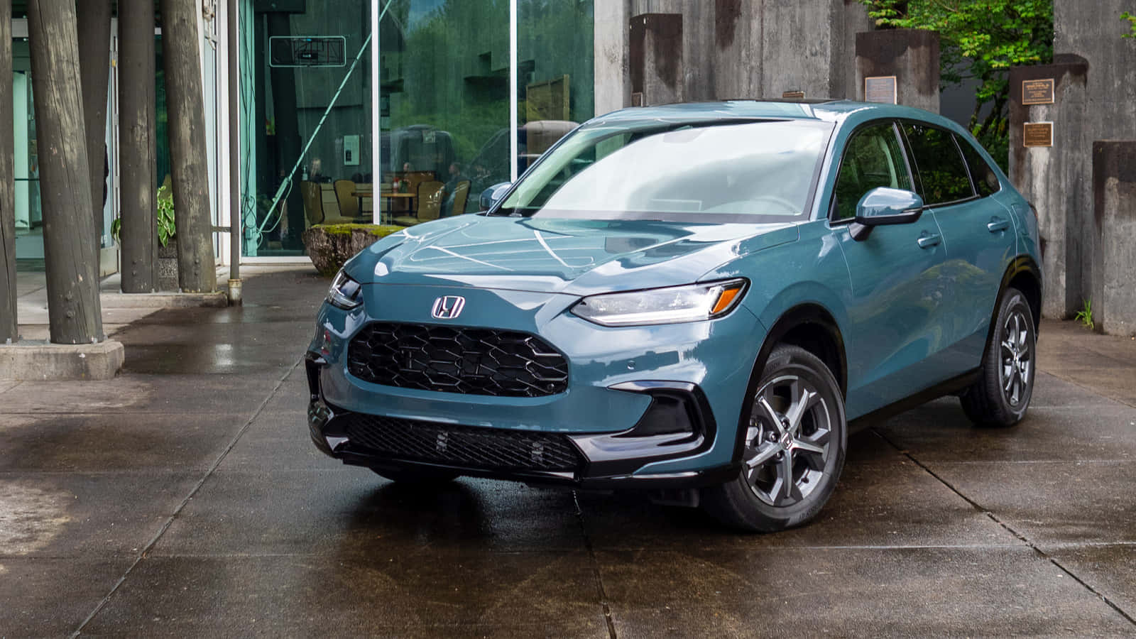 Honda Hr-v 桌布 壁紙 — 一輛時尚的青綠色本田SUV停放在濕漉漉的混凝土車道上，旁邊是現代玻璃建築，背景有樹木。