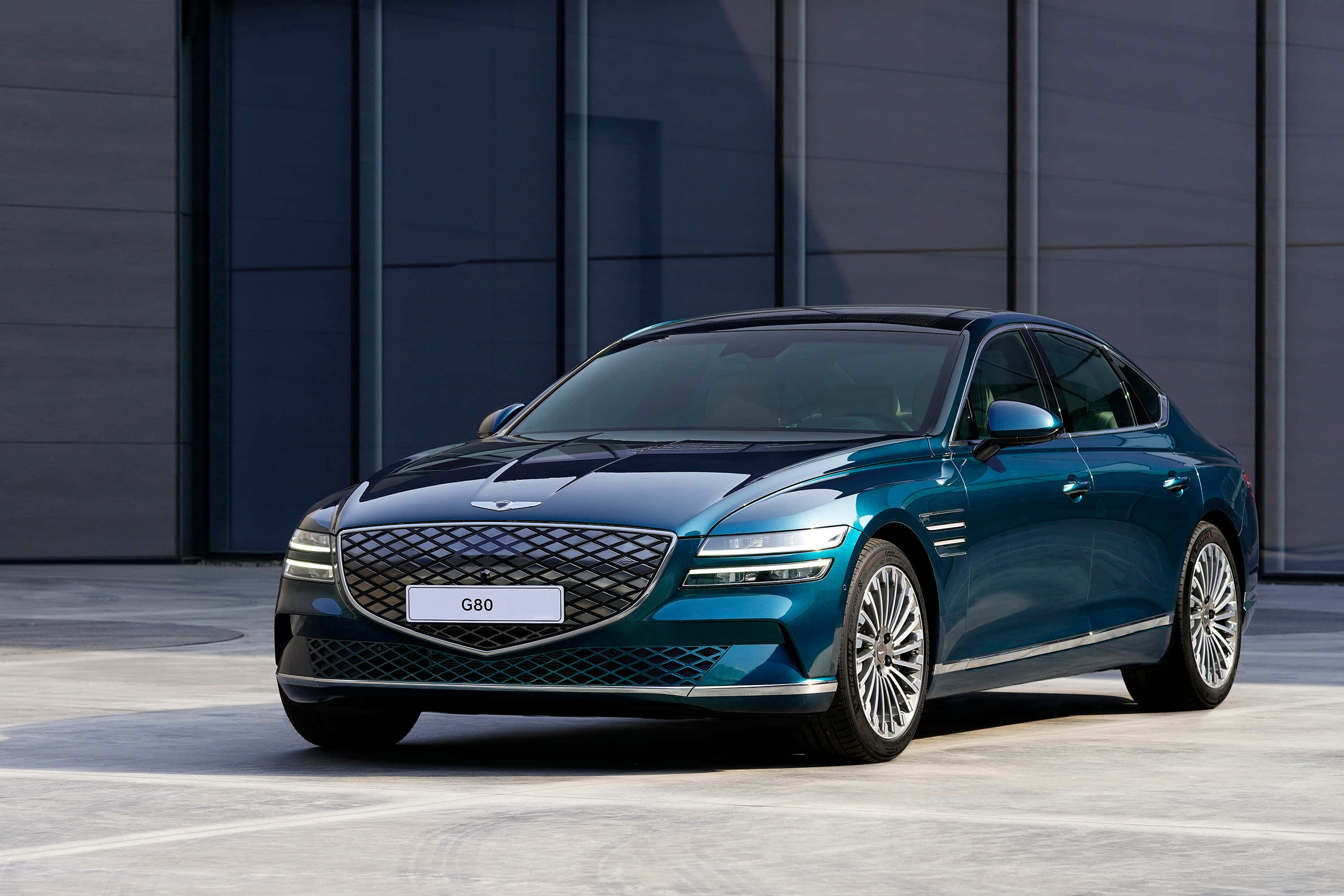 Genesis G80 桌布 壁紙 — 一輛時尚的青色Genesis G80轎車在明亮的日光下，在現代灰色建築外牆前閃閃發光。