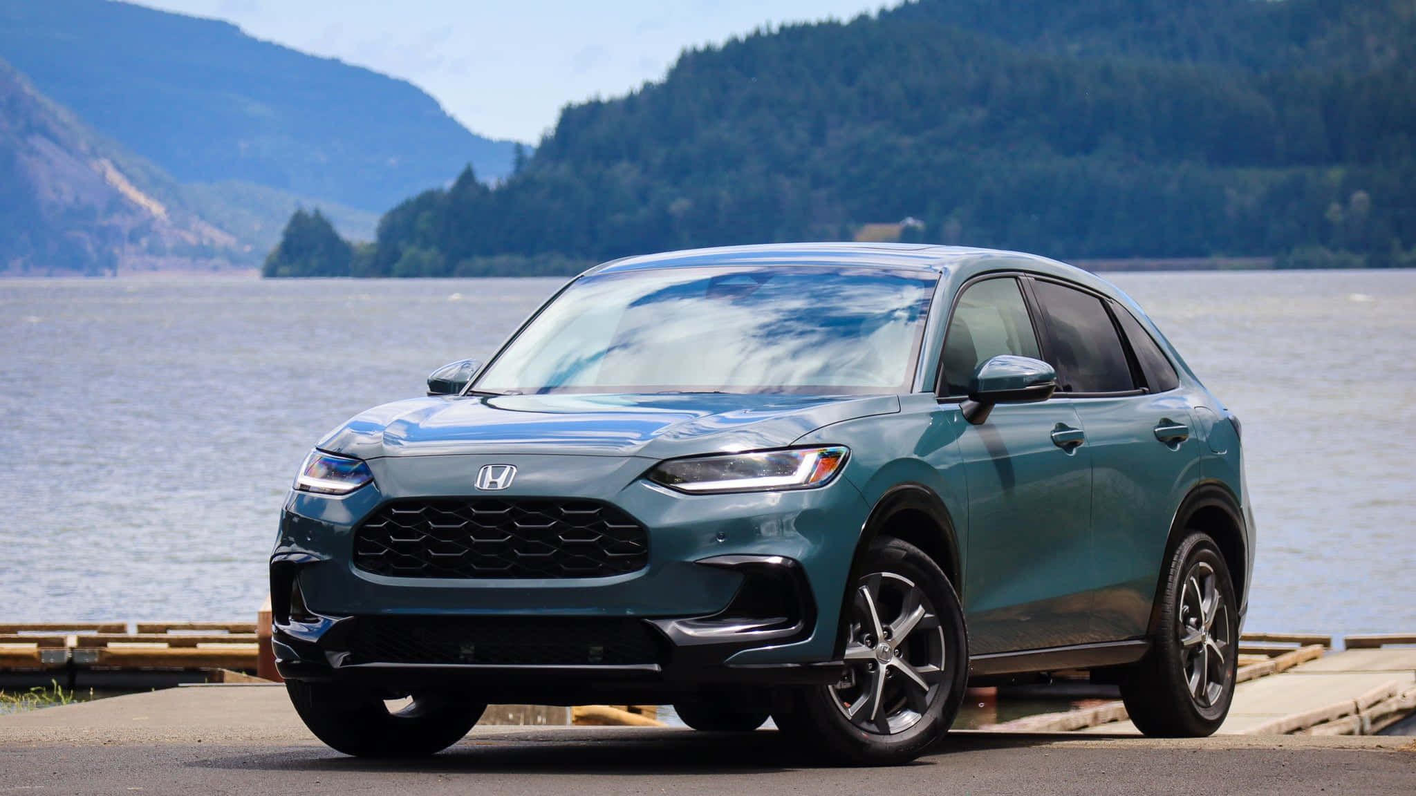 Honda Hr-v 桌布 壁紙 — 一輛時尚的青色本田SUV停泊在寧靜的湖邊，背景是森林覆蓋的山脈，天空晴朗。