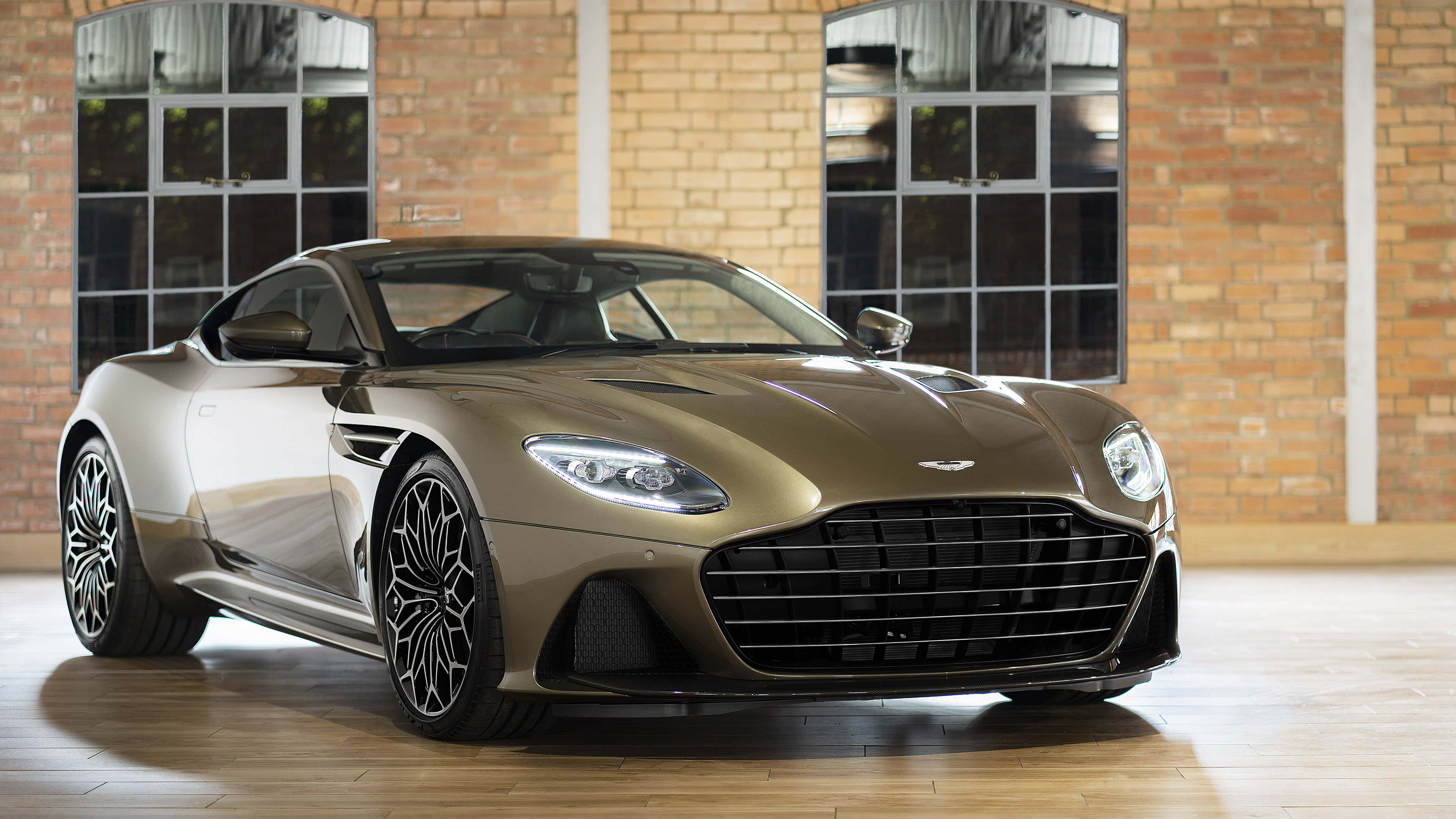 Aston Martin Dbs Superleggera 桌布 壁紙 — 一輛時尚的青銅色Aston Martin DB11在工作室燈光下，以帶有大窗戶的質樸磚牆為背景閃閃發光。