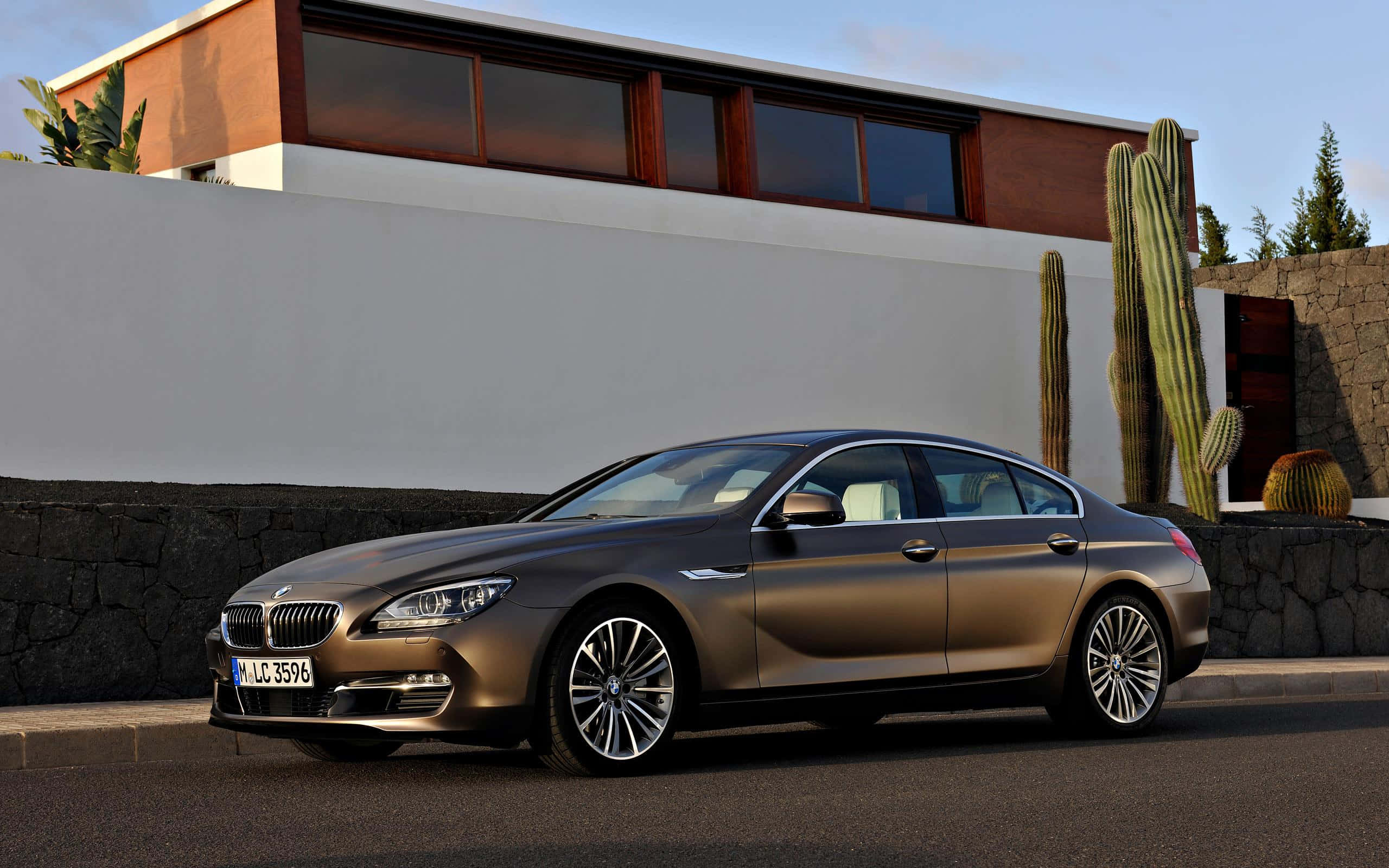 Bmw 6 Series 桌布 壁紙 — 一輛時尚的青銅色BMW 6系列轎車停在瀝青路上，旁邊是現代住宅，有仙人掌和石牆，天空晴朗。