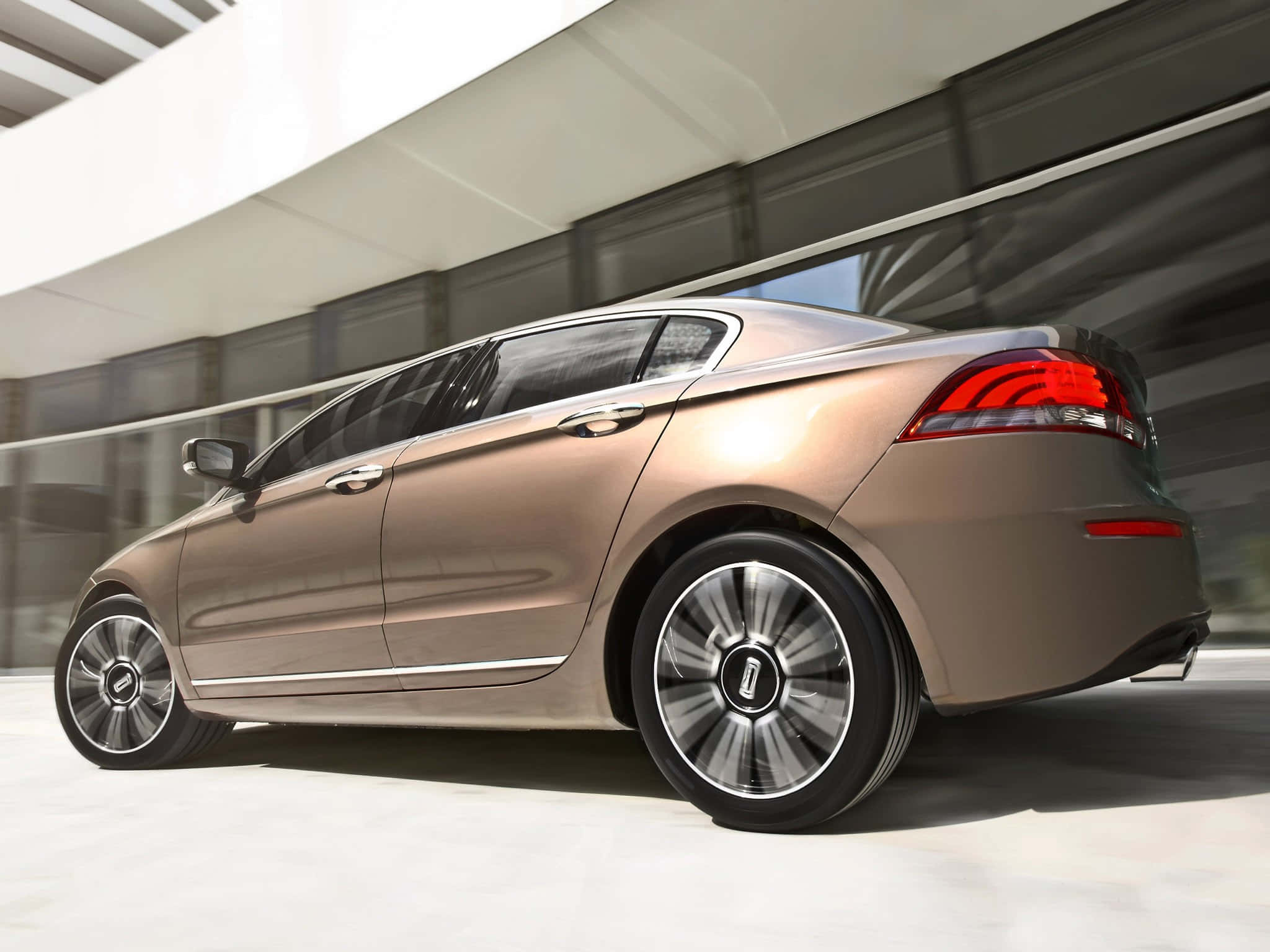 Qoros 桌布 壁紙 — 一輛時尚的青銅色轎車滑過現代玻璃建築，動態模糊效果強調速度與奢華。