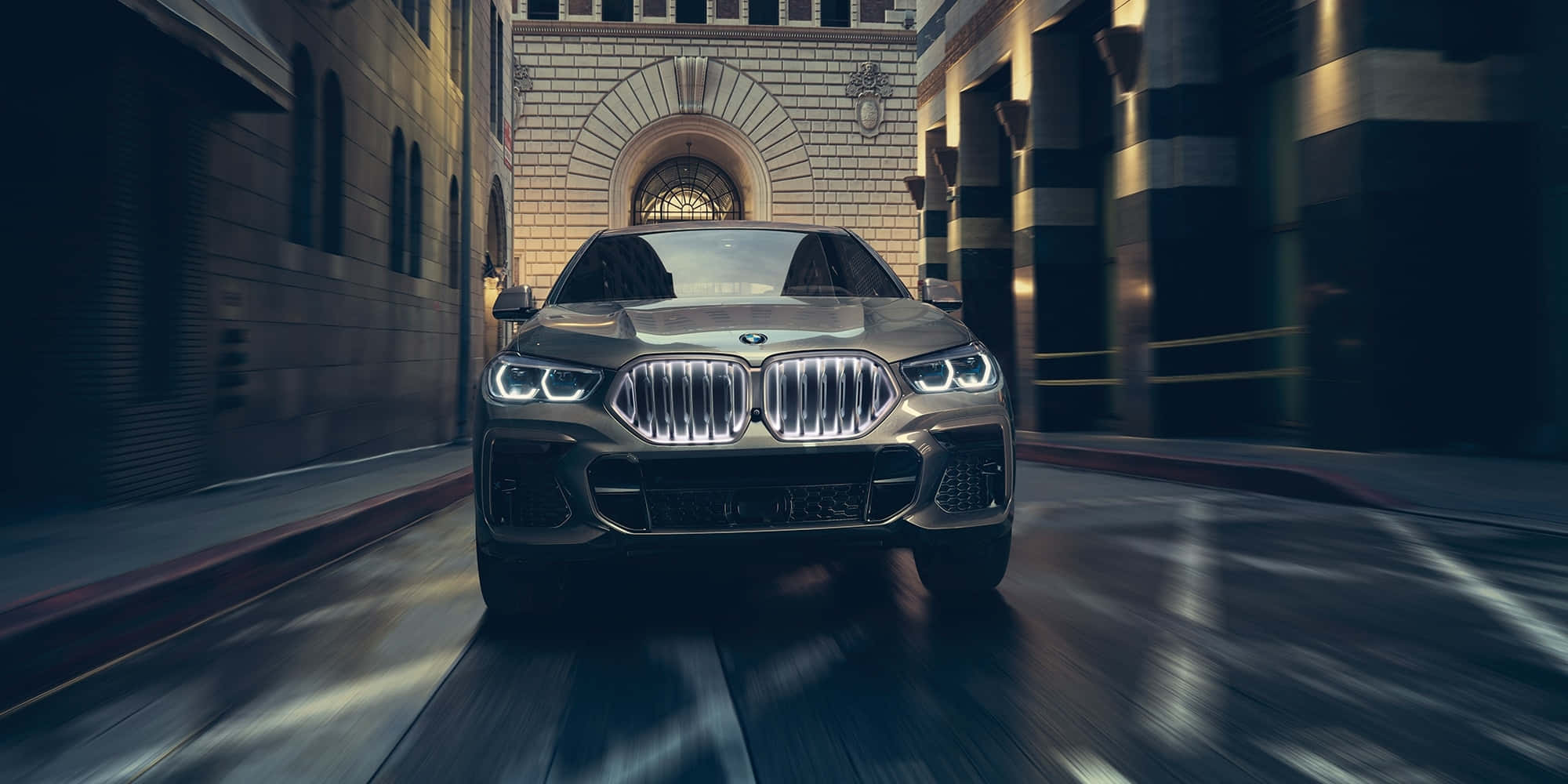 Bmw X6 M 桌布 壁紙 — 一輛時尚的黃金BMW SUV在狹窄的城市小巷中飛馳，帶有動態模糊和溫暖的建築照明。