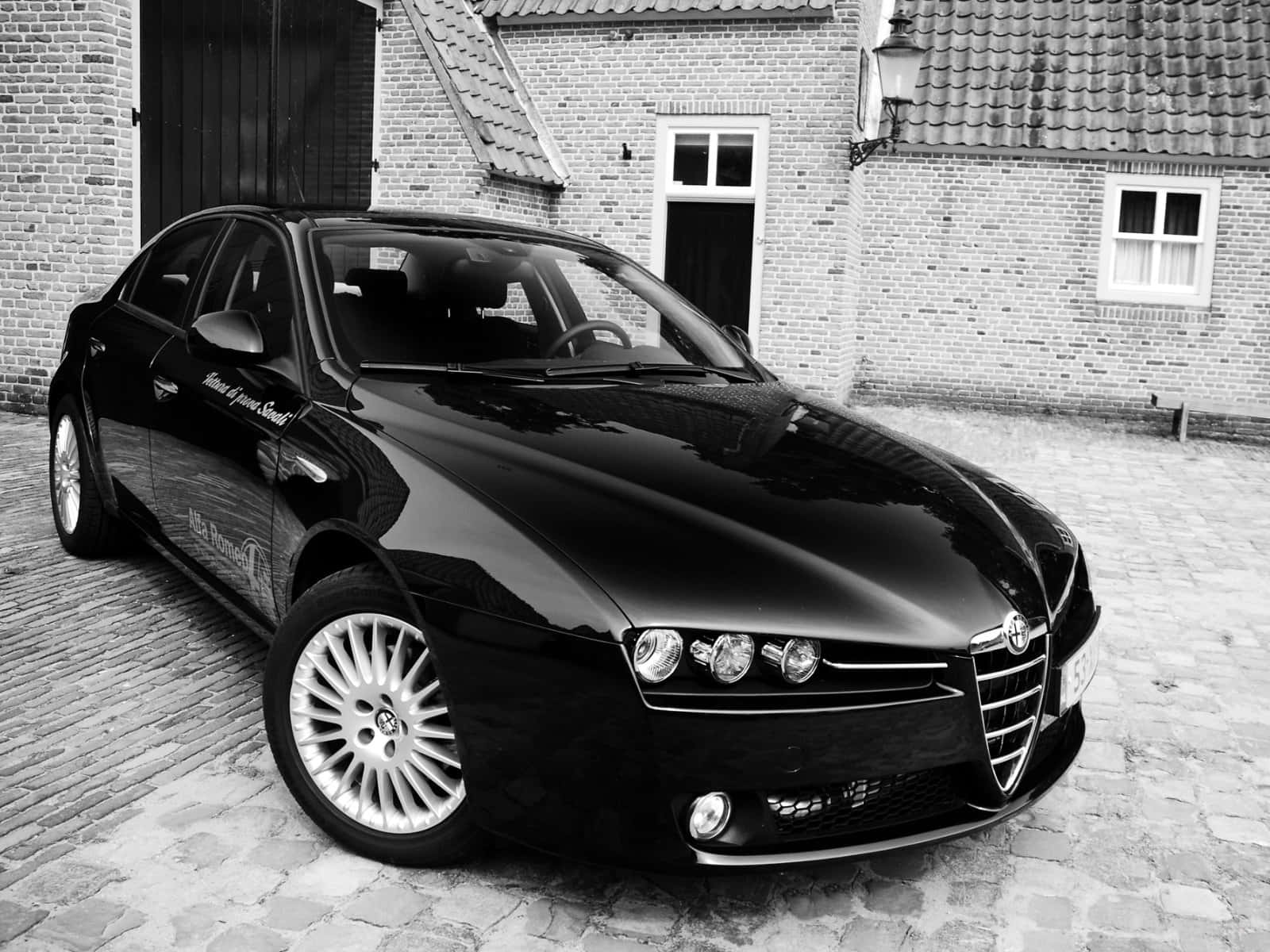 Alfa Romeo 159 桌布 壁紙 — 一輛時尚的黑色 Alfa Romeo 轎車在單色調的磚砌建築旁的鵝卵石庭院中閃閃發光。