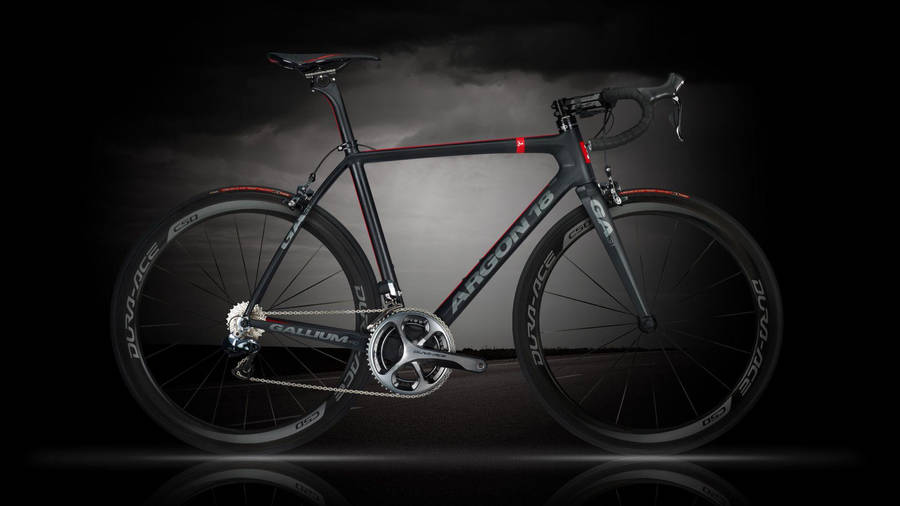 桌布 壁紙 — 一輛時尚的黑色 Argon 18 公路自行車，帶有紅色點綴，在暴風雨般的灰色天空背景下戲劇性地矗立。
