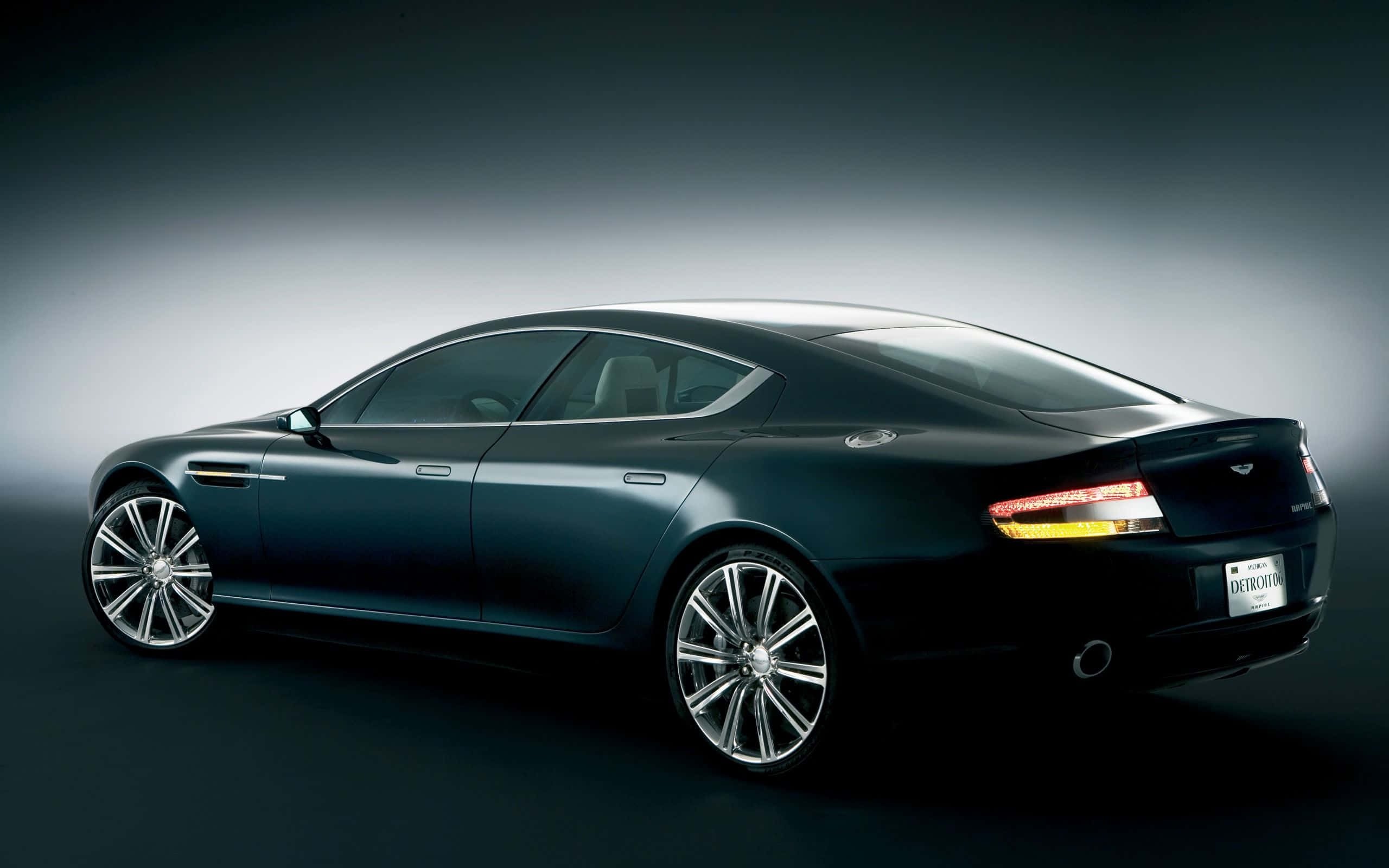 Aston Martin Rapide S 桌布 壁紙 — 一輛時尚的黑色 Aston Martin Rapide 在攝影棚燈光下閃耀，展現其優雅曲線和鍍鉻輪圈。