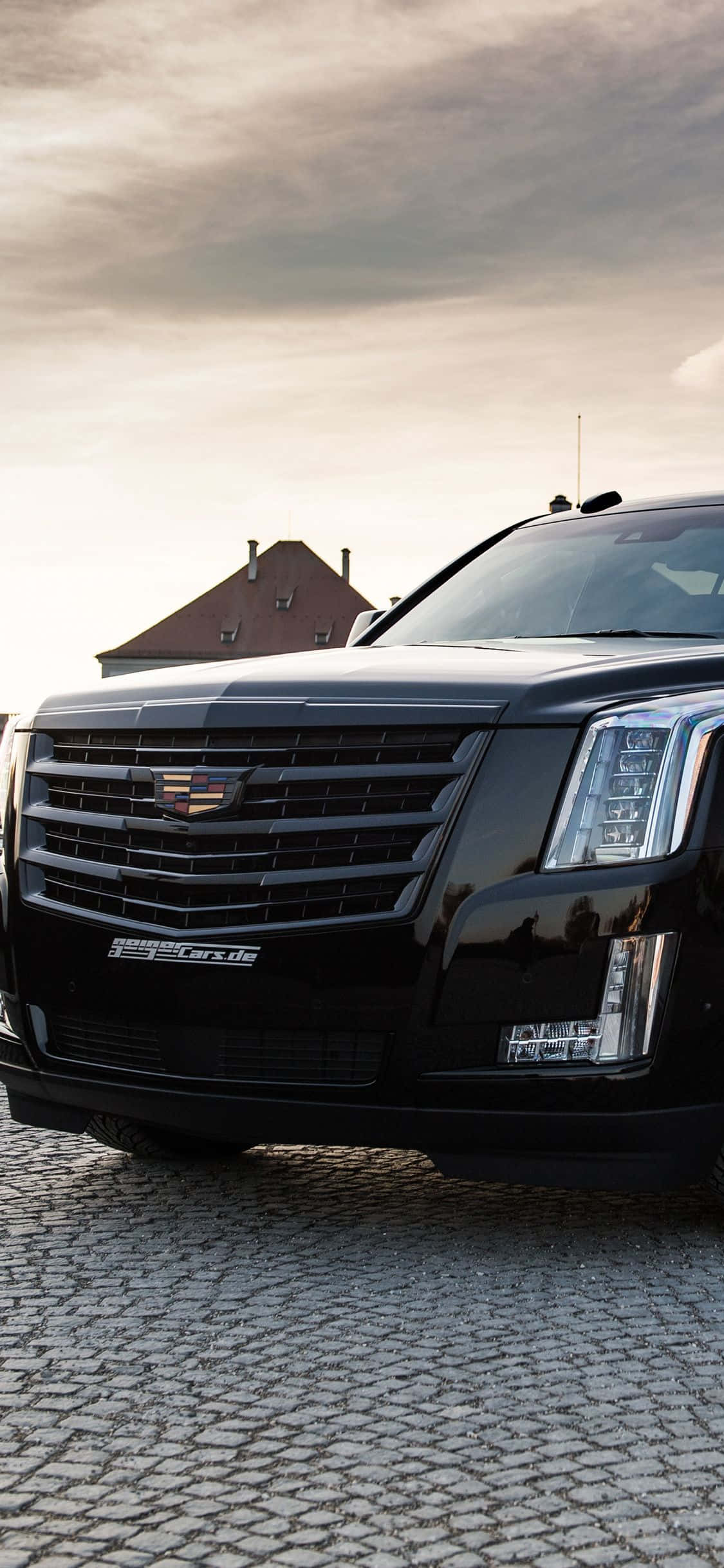 Cadillac Escalade 桌布 壁紙 — 一輛時尚的黑色 Cadillac Escalade 停泊在鵝卵石街道上，天空多雲，背景有一間房屋。