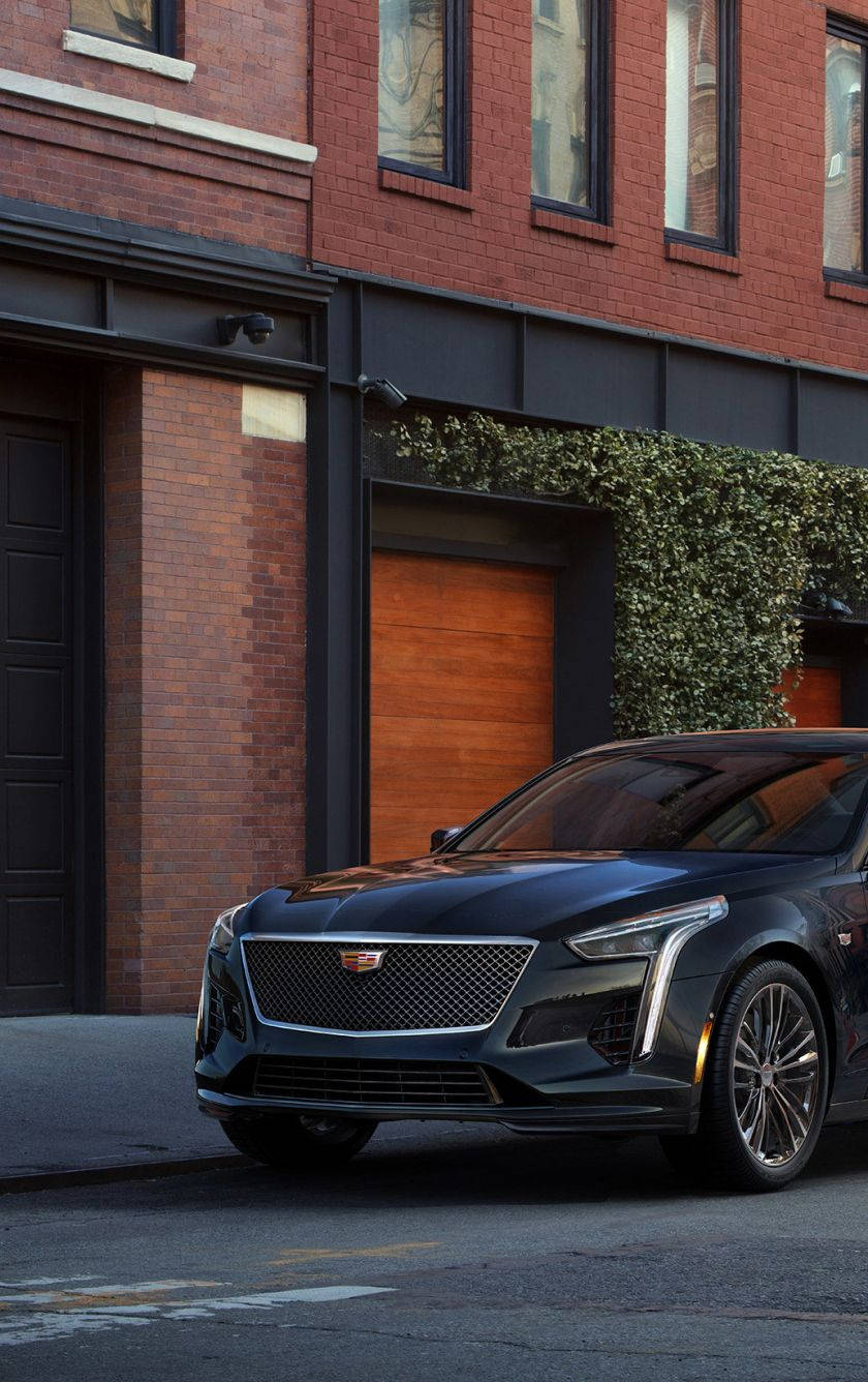 凱迪拉克 iPhone 桌布 壁紙 — 一輛時尚的黑色 Cadillac CT4-V 停放在城市街道上，旁邊是一棟有綠色常春藤的紅磚建築。