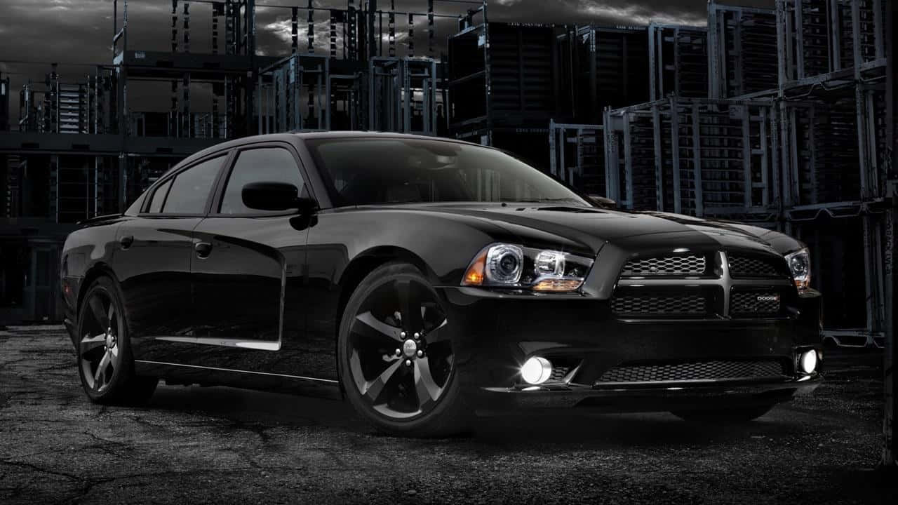 Dodge Charger 桌布 壁紙 — 一輛時尚的黑色 Dodge Charger 停放在風暴天空下的粗糙工業倉庫中。