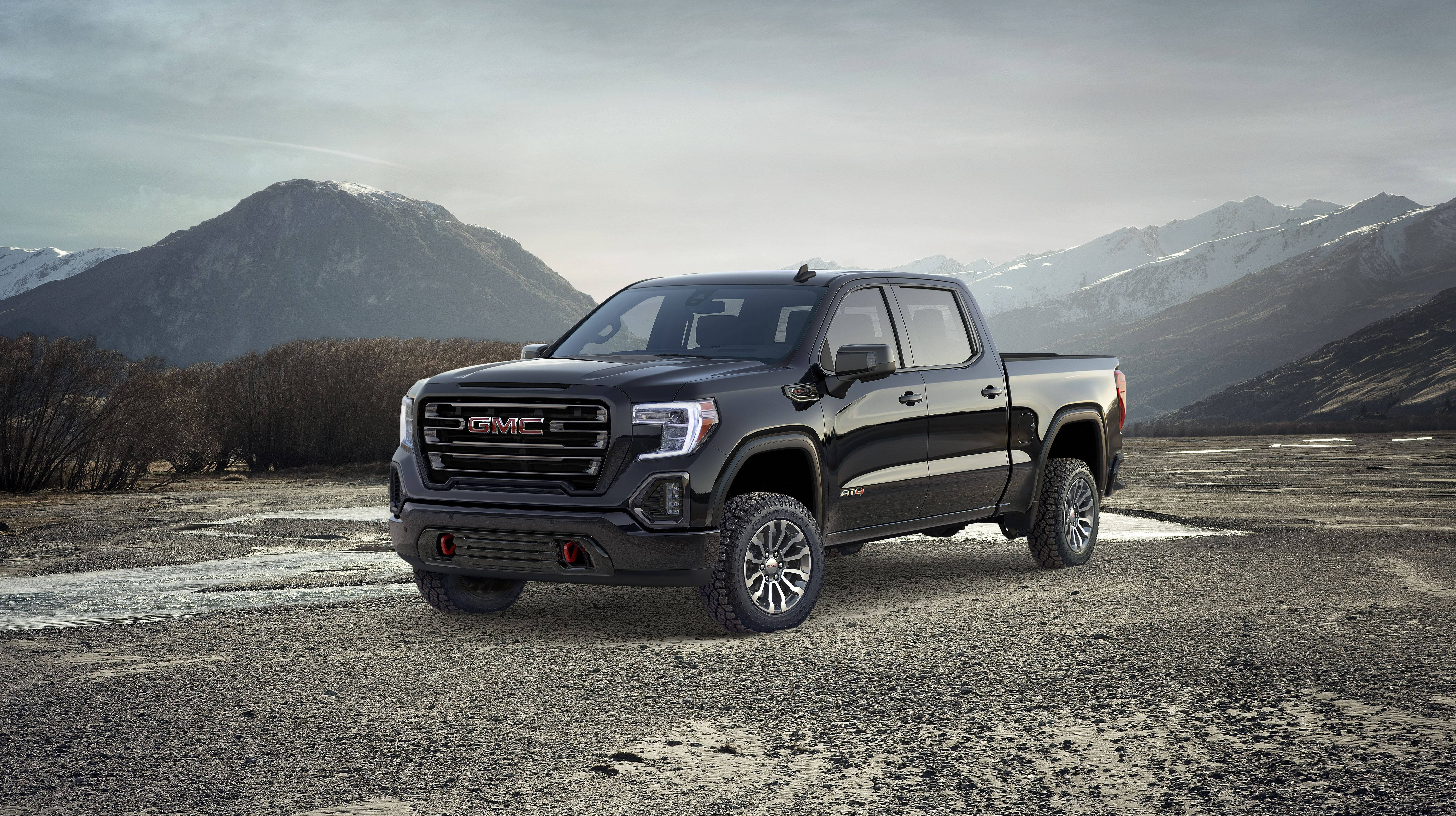 Gmc 桌布 壁紙 — 一輛時尚的黑色 GMC Sierra 皮卡車停泊在礫石平原上，背後有積雪的山峰在陰天中聳立。