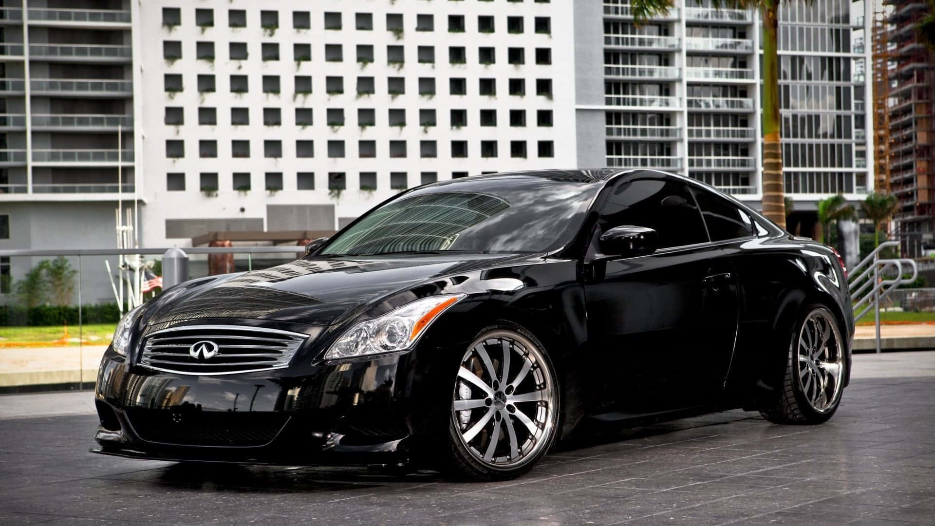 Black Car 桌布 壁紙 — 一輛時尚的黑色 Infiniti G Coupe 在日光下閃耀，停泊在現代建築物和棕櫚樹背景的城市街道上。