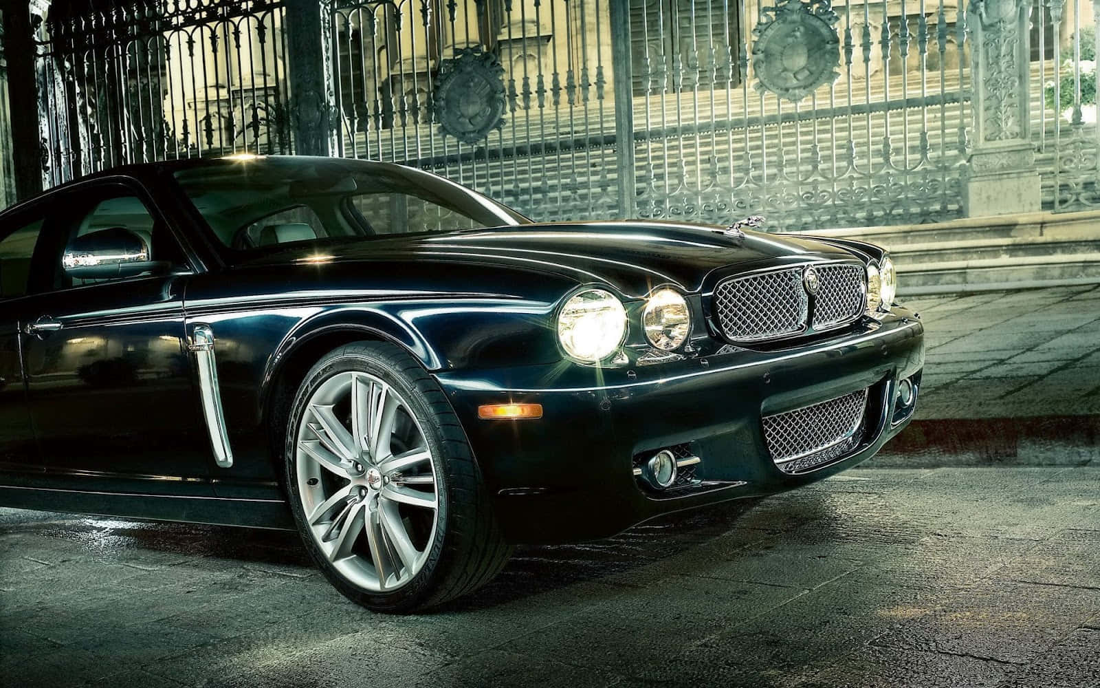 Jaguar X-type 桌布 壁紙 — 一輛時尚的黑色 Jaguar XK8 跑車在街燈下閃閃發光，停在華麗的鍛鐵門前。