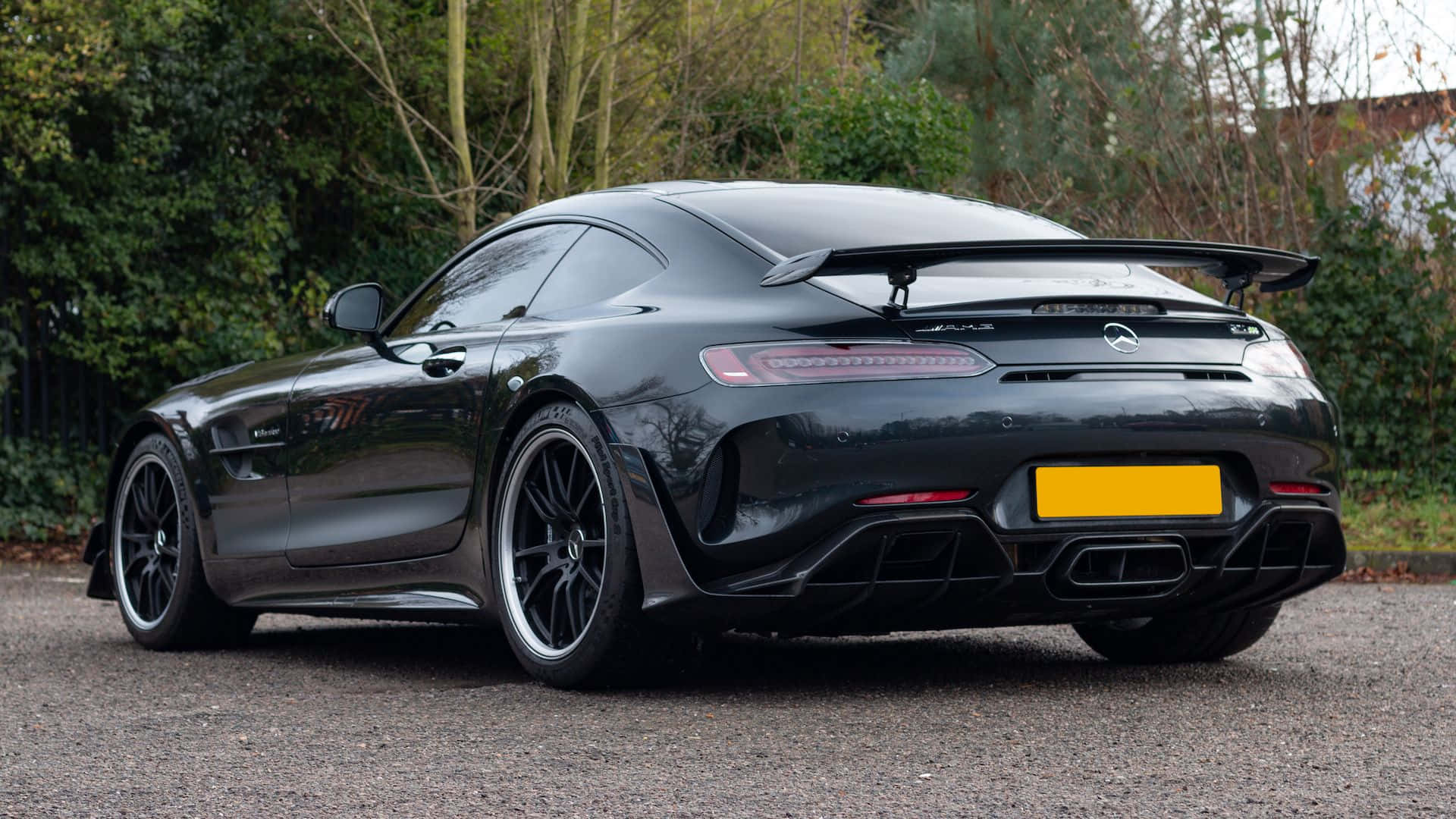 汽車 桌布 壁紙 — 一輛時尚的黑色 Mercedes-AMG GT R 跑車停在碎石地上，背景有樹木。