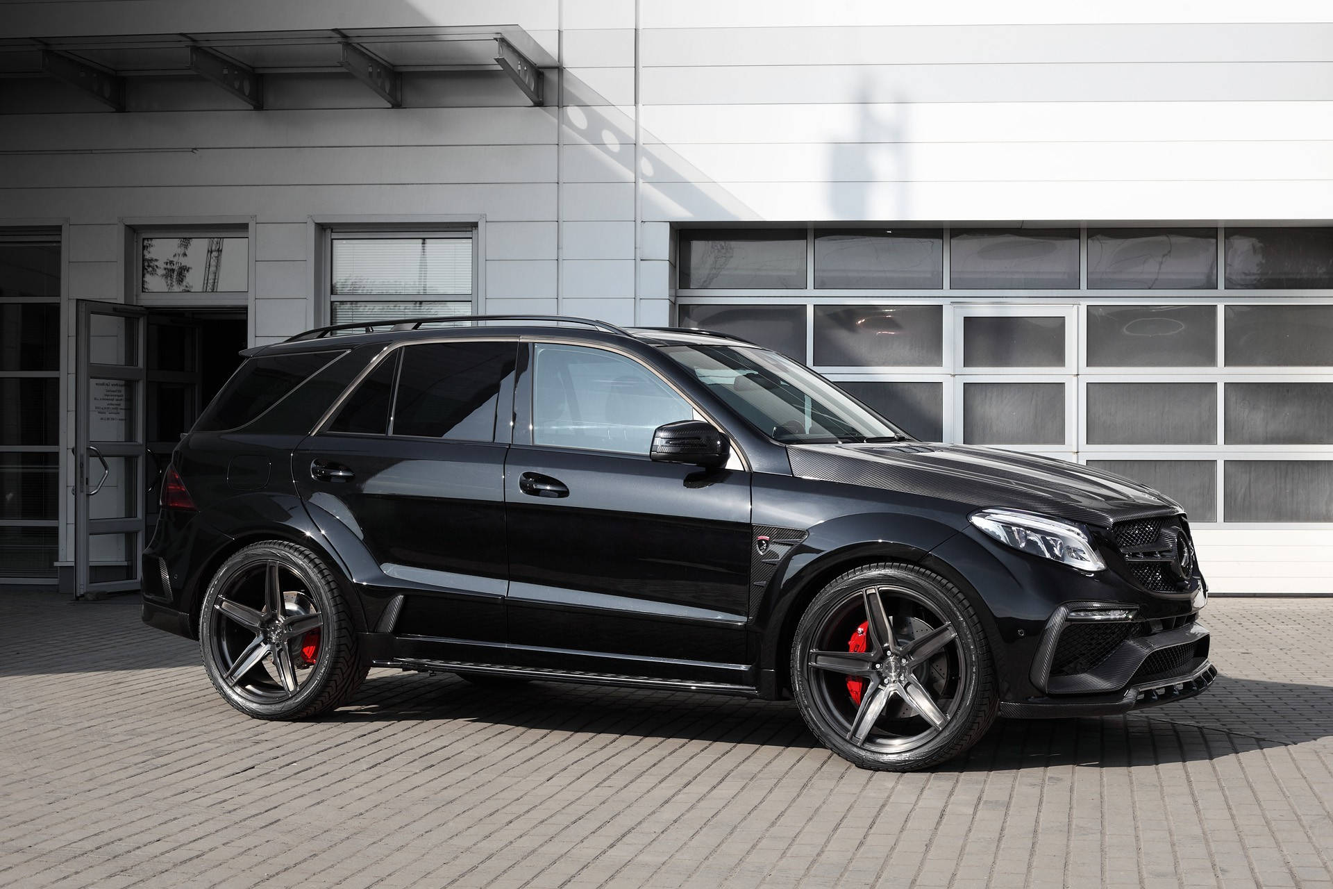 benz 4K 桌布 壁紙 — 一輛時尚的黑色 Mercedes-AMG SUV，帶有紅色制動卡鉗，停在現代建築前的鋪砌庭院中。