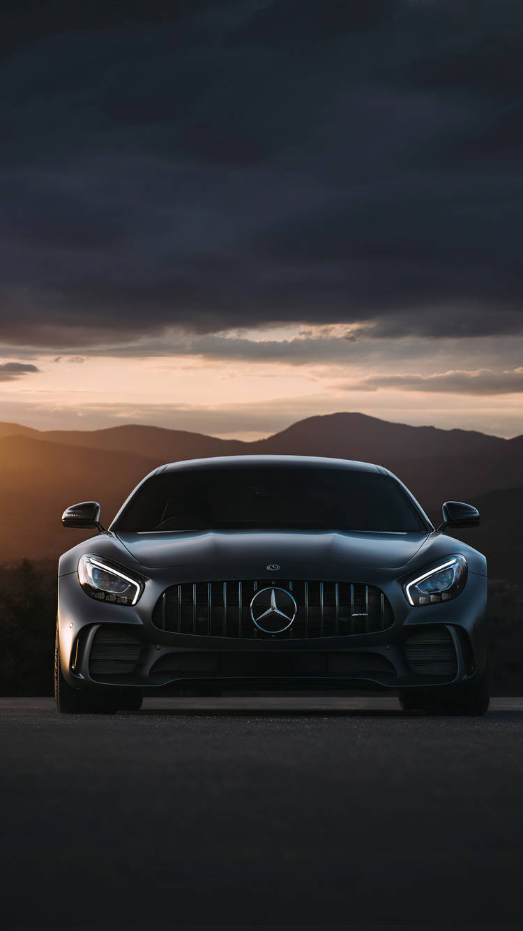 AMG iPhone 桌布 壁紙 — 一輛時尚的黑色 Mercedes-AMG GT 跑車在戲劇性的暮色天空和山脈背景下向前行駛。