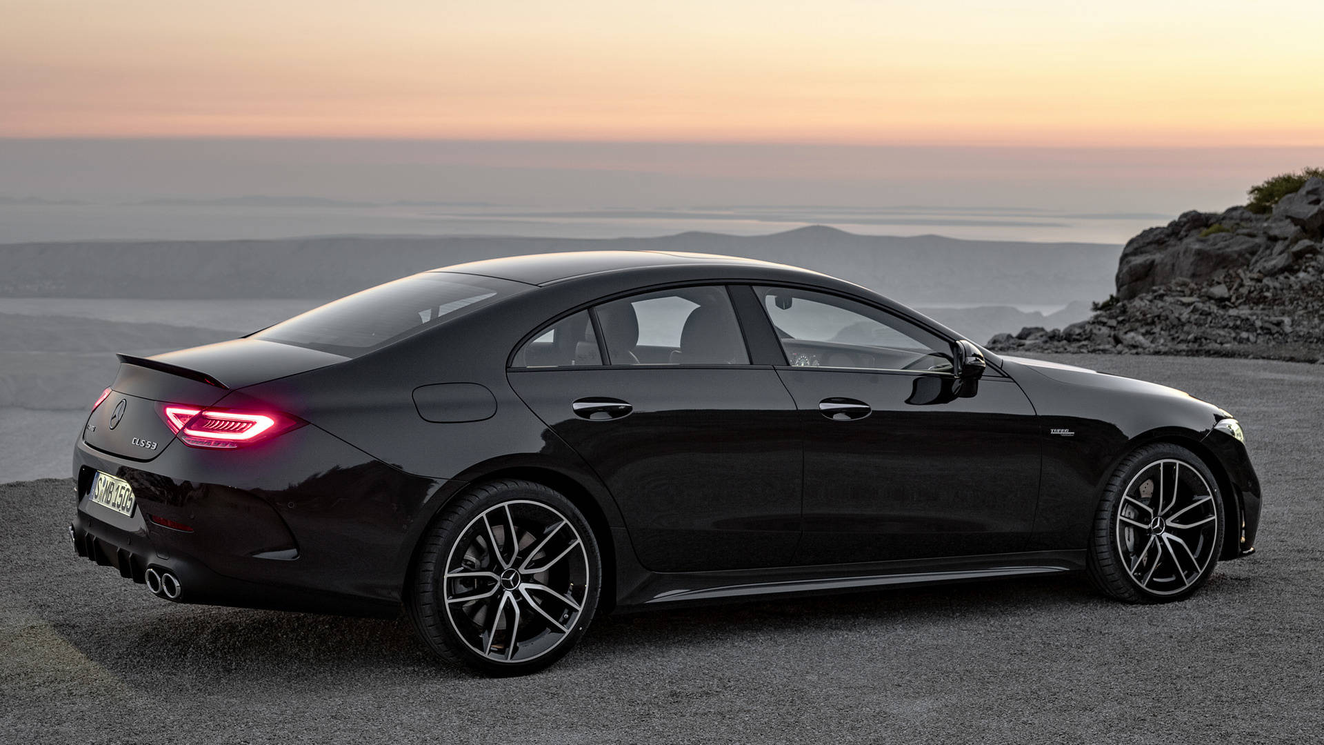 Mercedes Amg 桌布 壁紙 — 一輛時尚的黑色 Mercedes-AMG CLS450 轎跑車停在日落時分的海岸懸崖上，尾燈閃閃發光。