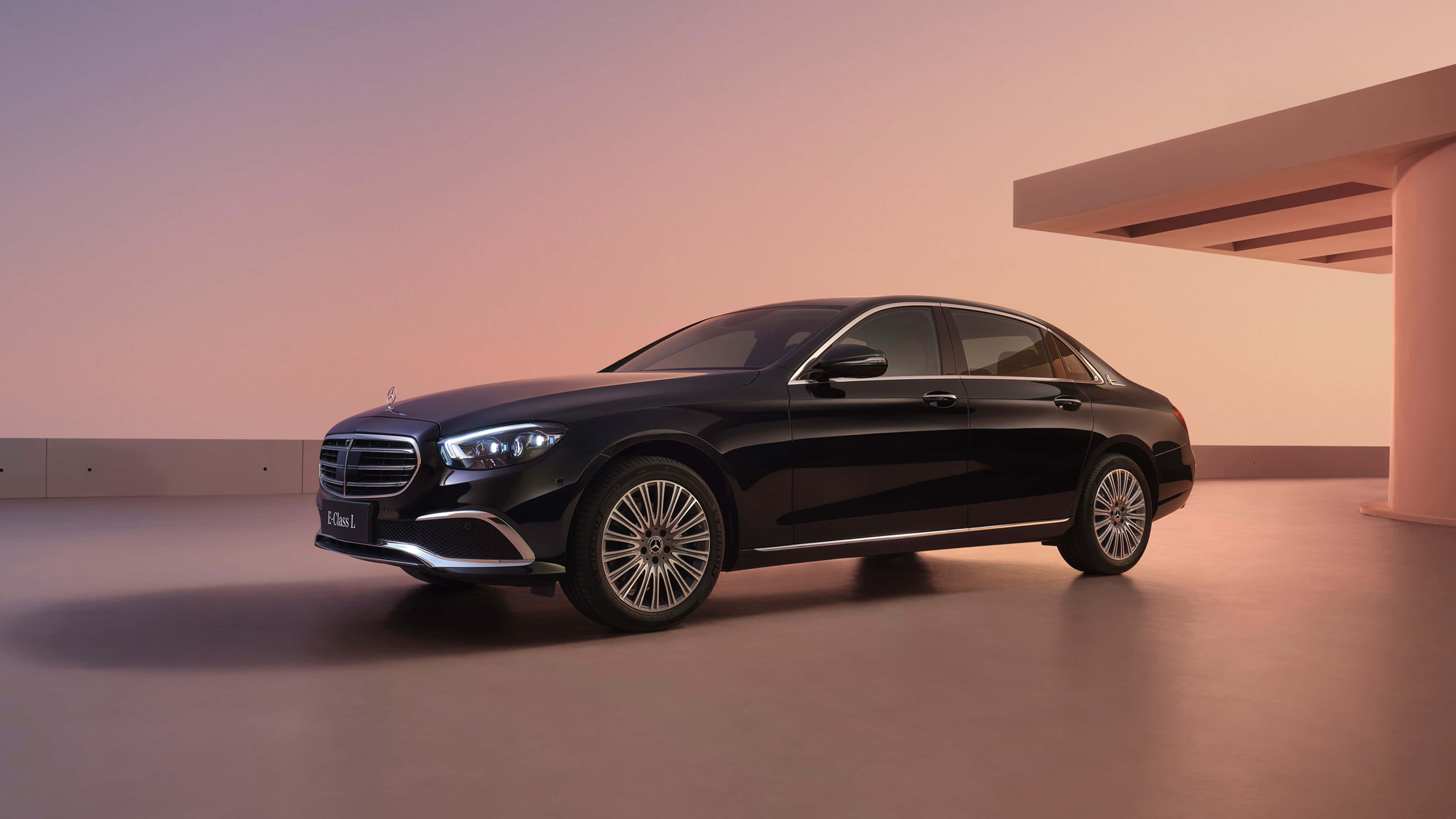 Mercedes Benz Clase E 桌布 壁紙 — 一輛時尚的黑色 Mercedes-Maybach S-Class 轎車在溫暖的暮色燈光下，於極簡現代建築環境中閃耀。
