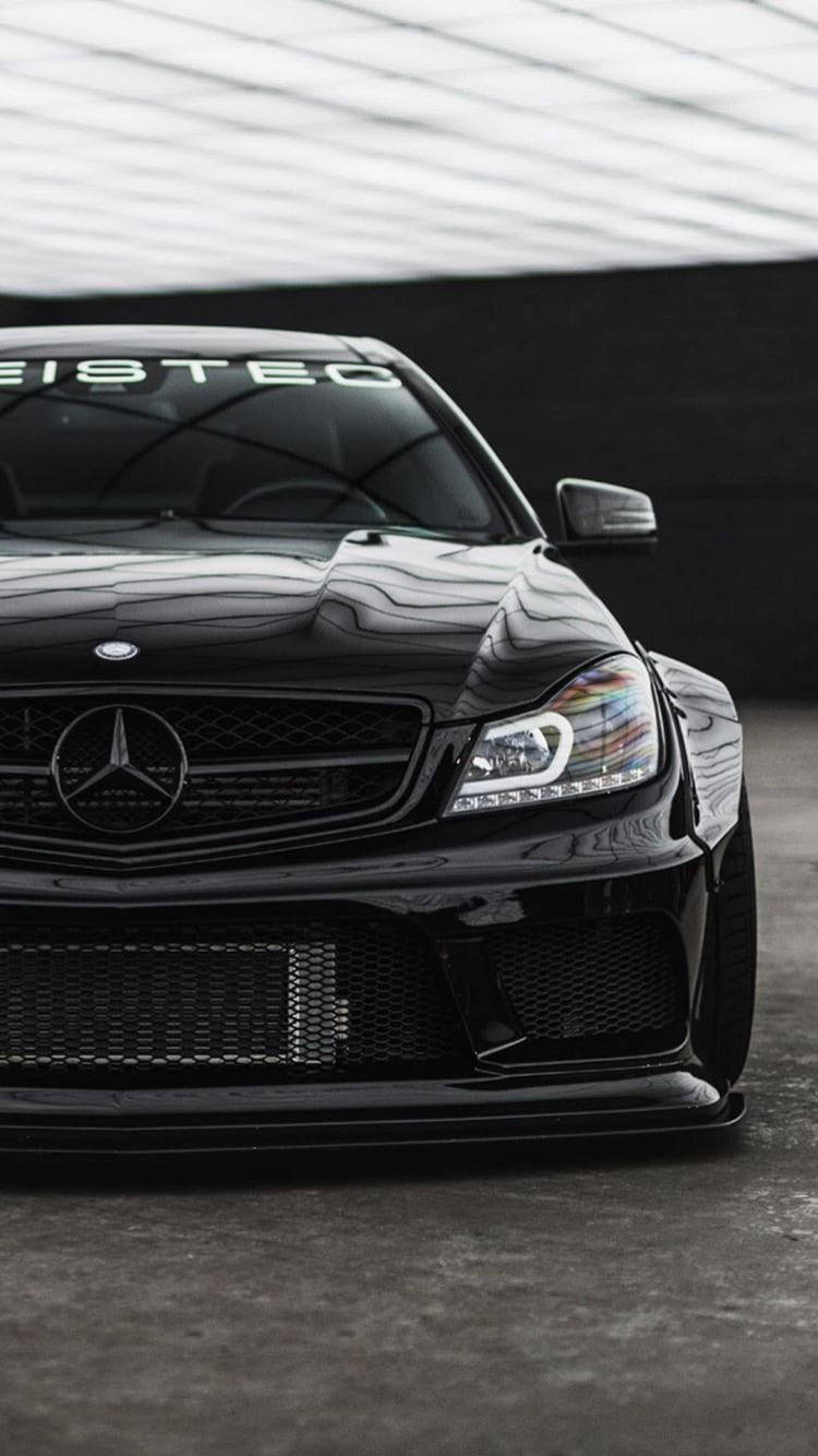 mercedes amg iPhone 桌布 壁紙 — 一輛時尚的黑色 Mercedes 跑車，具有侵略性造型和自訂改裝，停放在白色遮陽篷下。