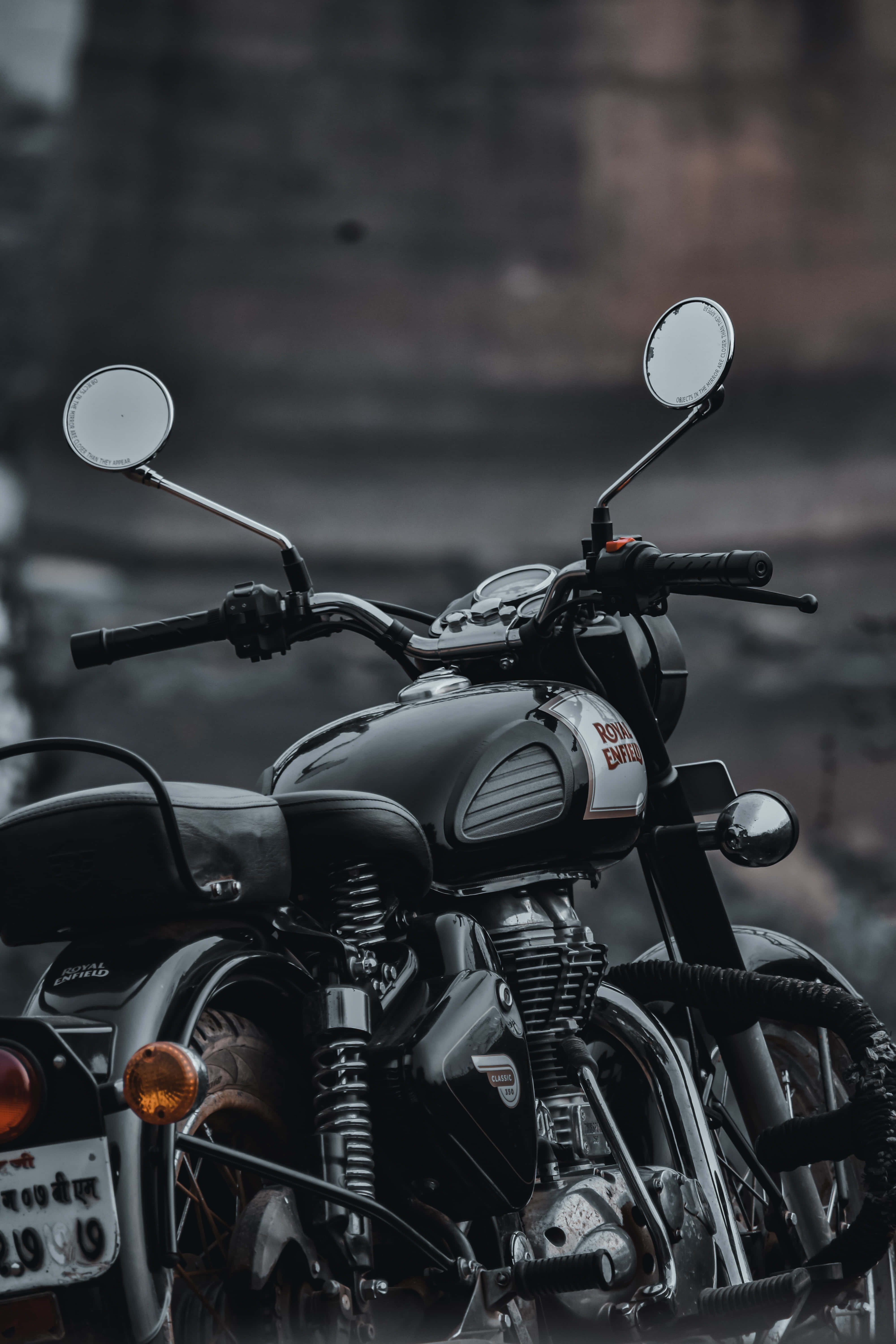 腳踏車 桌布 壁紙 — 一輛時尚的黑色 Royal Enfield 機車，帶有鍍鉻裝飾和圓形後視鏡，在模糊的城市背景下蓄勢待發。