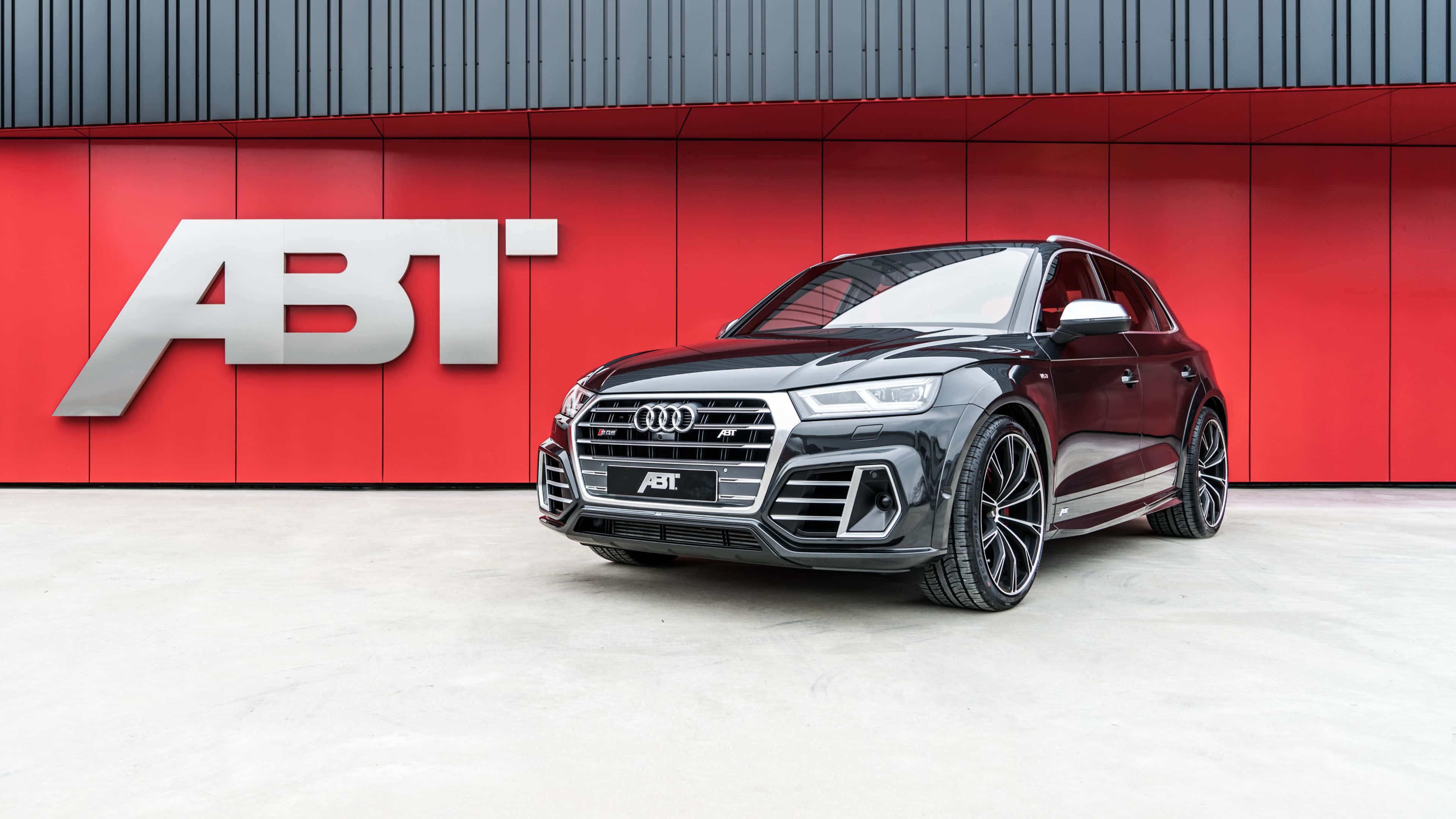 Audi Sq5 桌布 壁紙 — 一輛時尚的黑色ABT改裝奧迪SQ5 SUV，停在搶眼的紅色牆前，牆上有銀色ABT標誌。