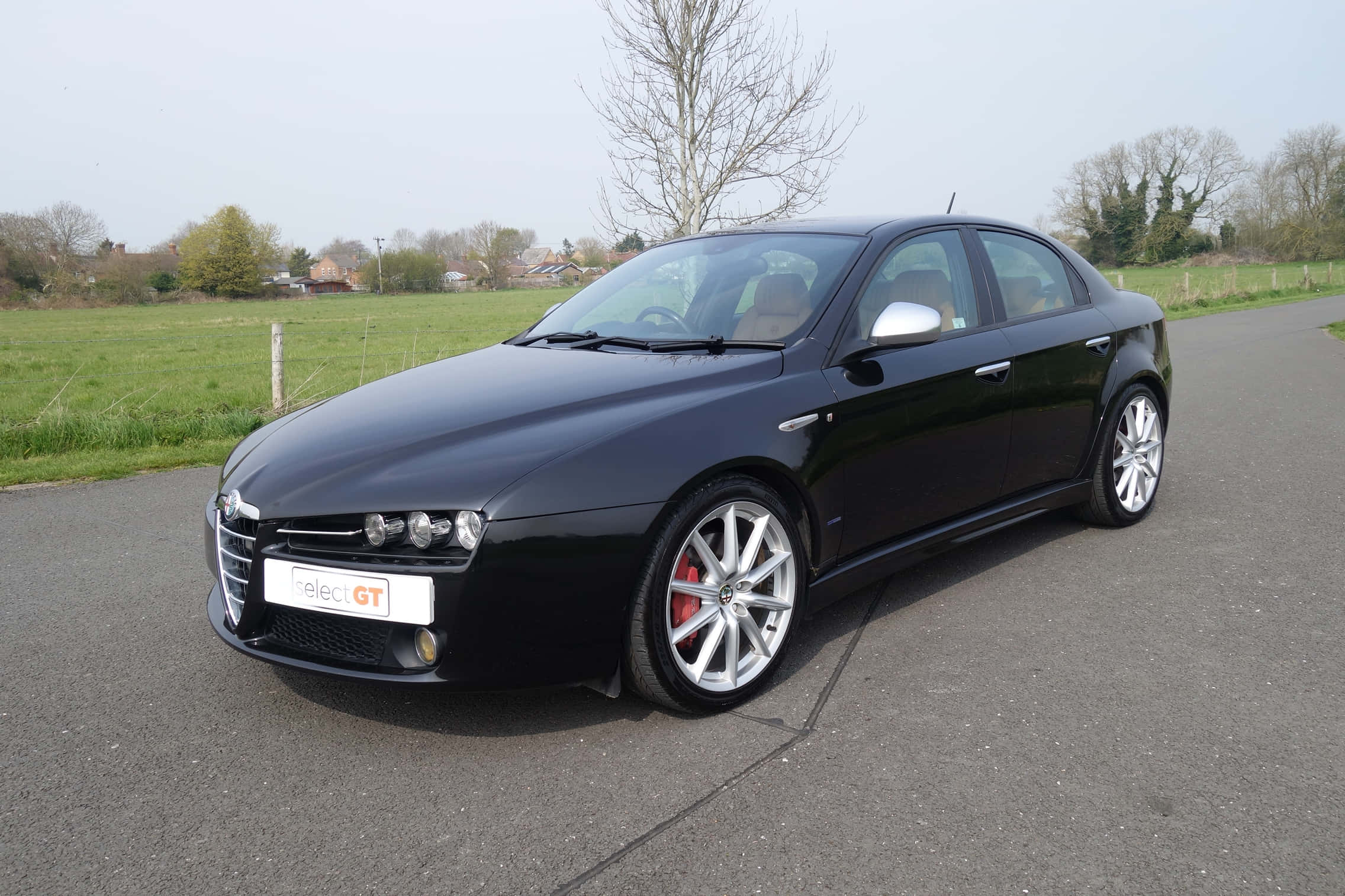 Alfa Romeo 159 桌布 壁紙 — 一輛時尚的黑色Alfa Romeo轎車，配備銀色輪圈和紅色制動卡鉗，停在鄉村道路旁，旁邊是綠色田野。