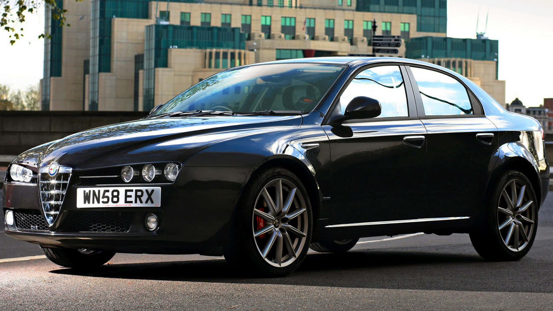 Alfa Romeo 159 桌布 壁紙 — 一輛時尚的黑色Alfa Romeo轎車在日光下閃耀，背景是現代建築的城市街道。