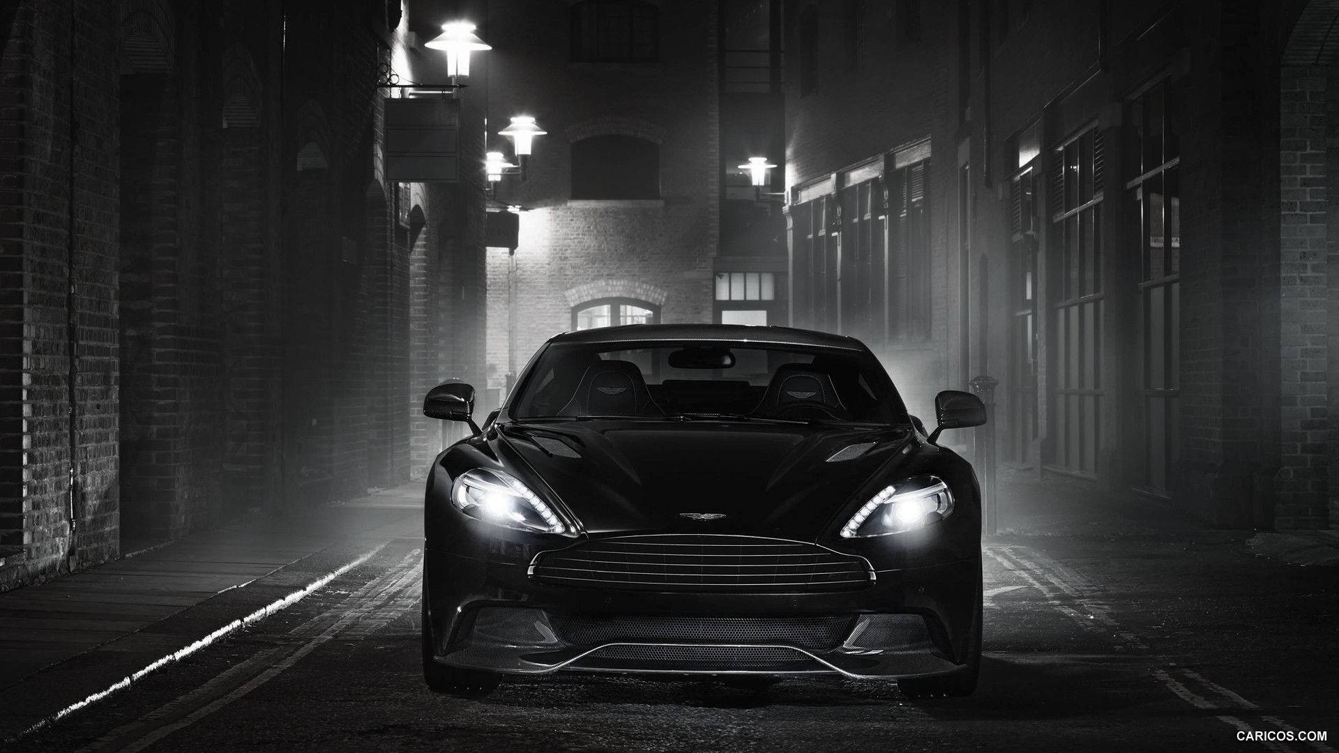 奧斯頓馬丁 桌布 壁紙 — 一輛時尚的黑色Aston Martin跑車在夜間霧濛濛的狹窄小巷中閃爍著車頭燈。