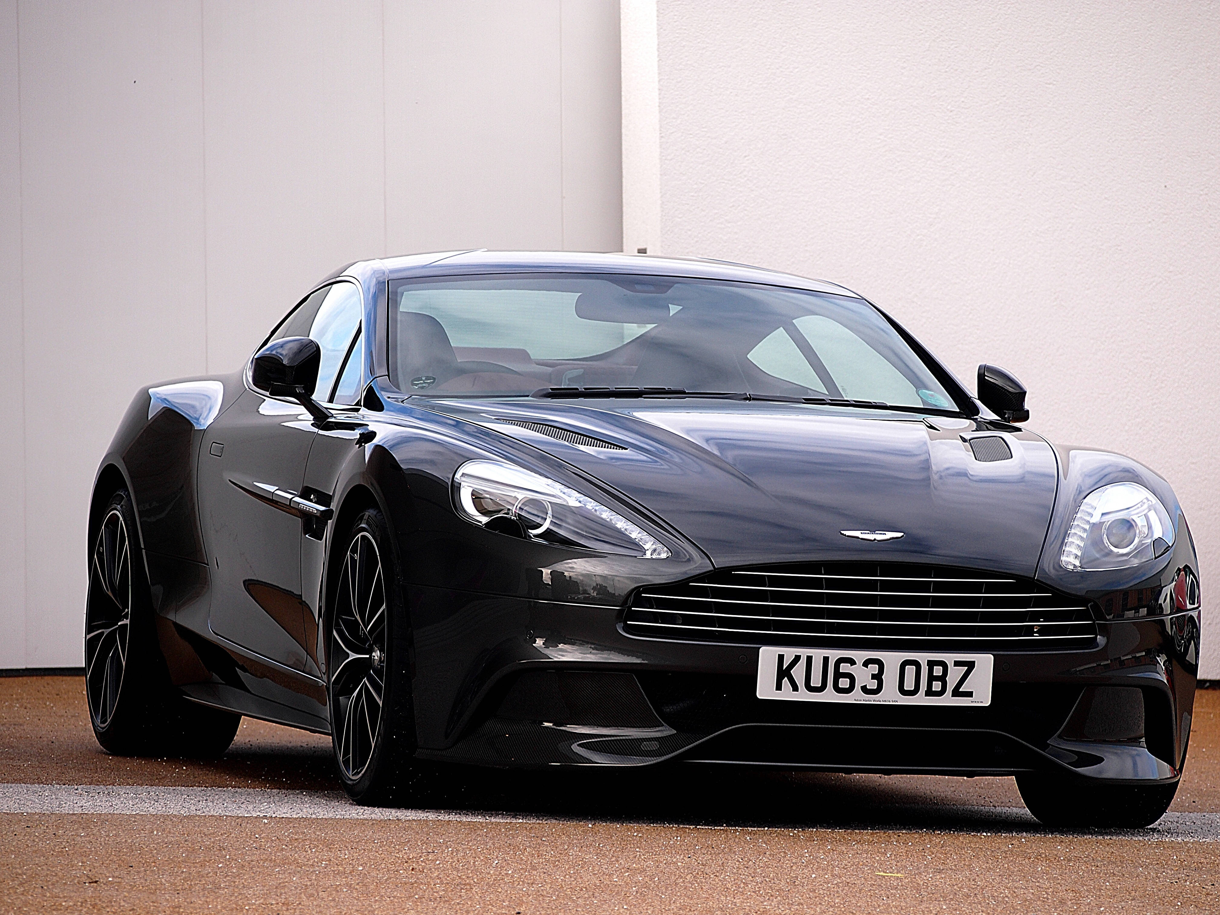 奧斯頓馬丁 桌布 壁紙 — 一輛時尚的黑色Aston Martin跑車在明亮的日光下閃閃發光，背景是簡約的白色牆壁。