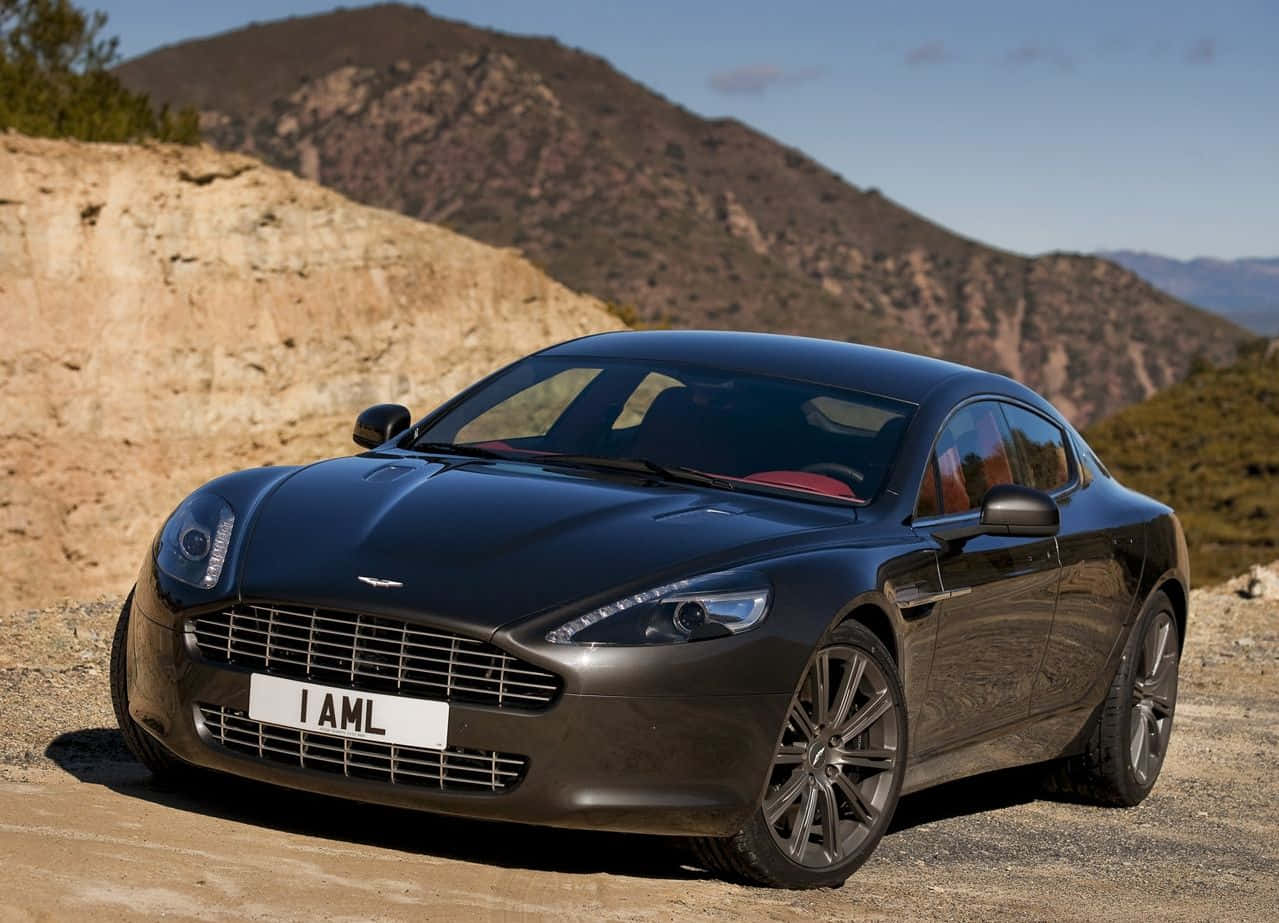 Aston Martin Rapide S 桌布 壁紙 — 一輛時尚的黑色Aston Martin跑車停泊在塵土飛揚的山路上，背景是崎嶇的山丘和清澈的藍天。
