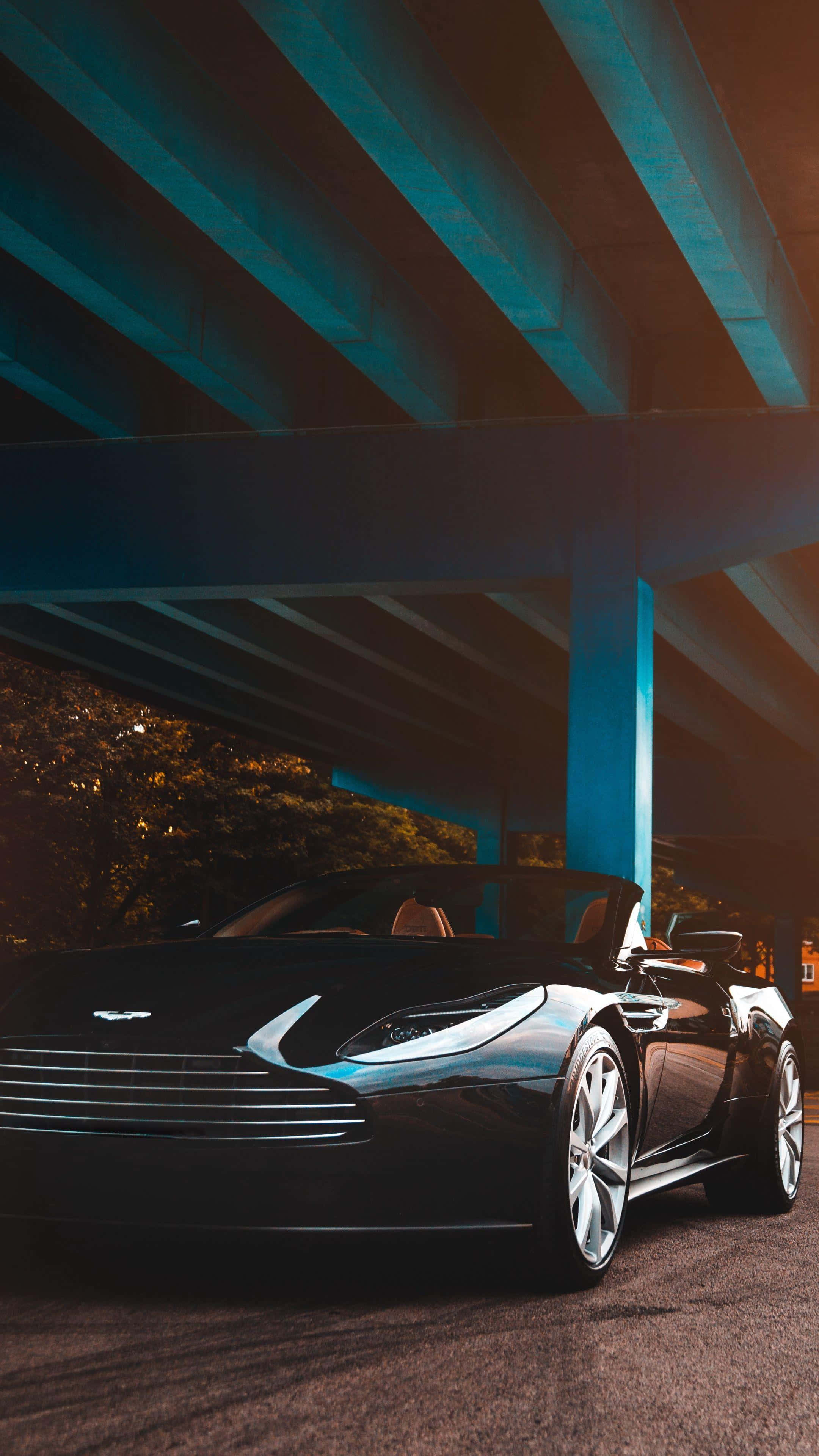 高清 桌布 壁紙 — 一輛時尚的黑色Aston Martin敞篷車在黃昏時停泊在發光的藍色橋下，周圍有溫暖的環境照明。
