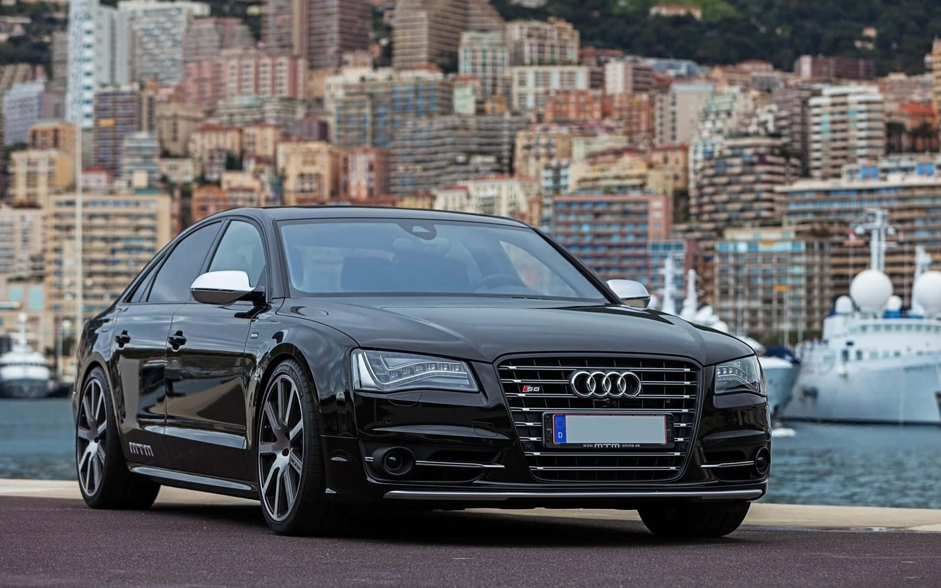 Audi S8 桌布 壁紙 — 一輛時尚的黑色Audi S8轎車停放在海濱，背景是密集的城市天際線和豪華郵輪。