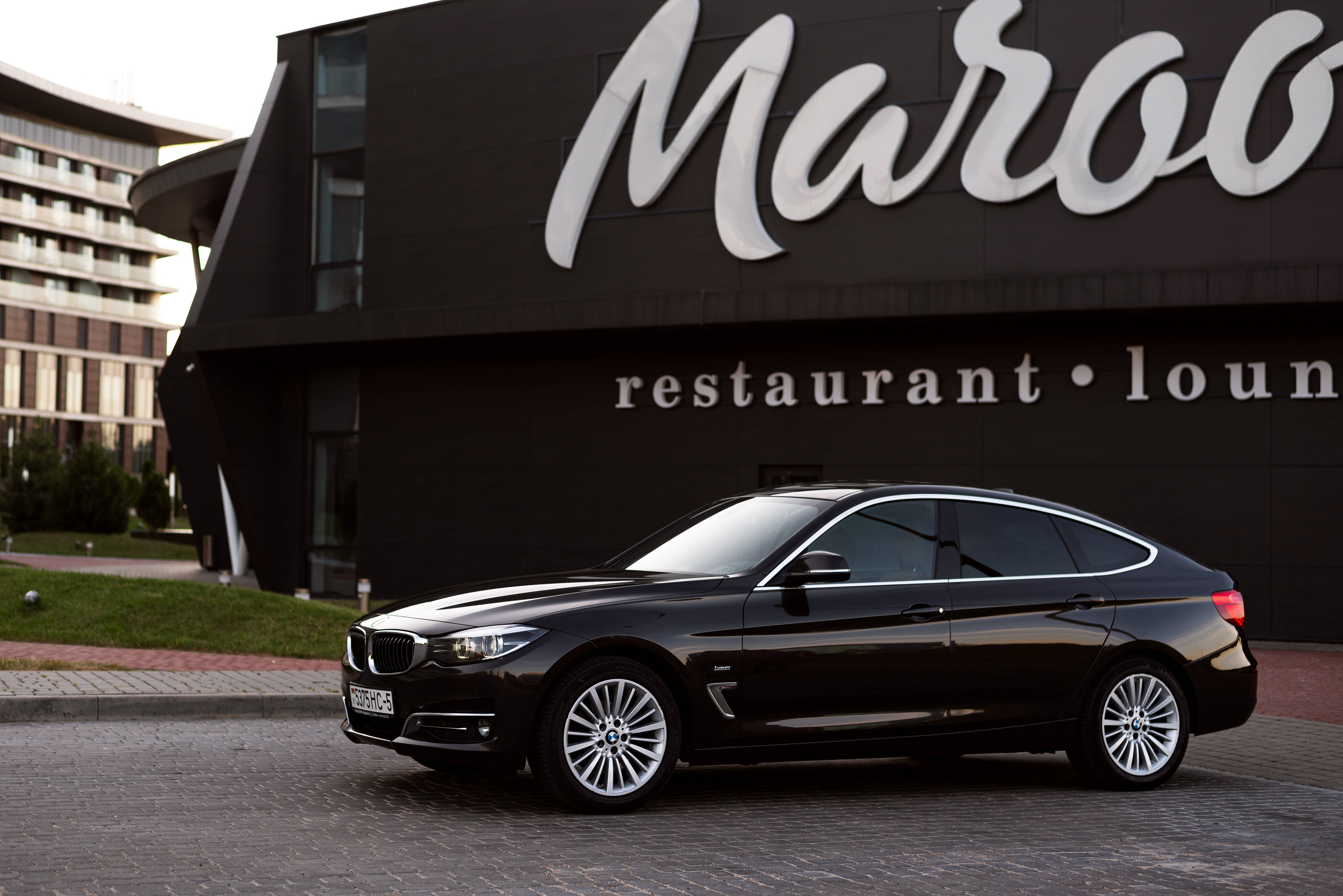 Black Bmw 桌布 壁紙 — 一輛時尚的黑色BMW Gran Coupe停在現代黑色建築前的鵝卵石車道上，建築物上有「Maroo restaurant lounge」標誌。