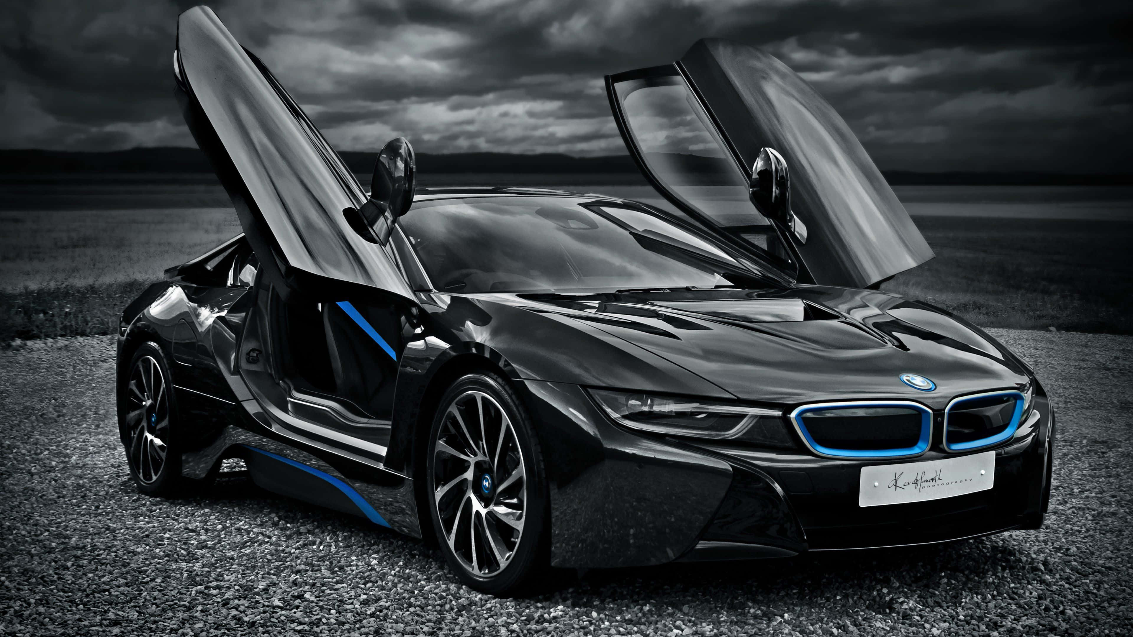 BMW 動圖 桌布 壁紙 — 一輛時尚的黑色BMW i8，鷗翼車門打開，停在碎石地上，天空陰沉多雲。