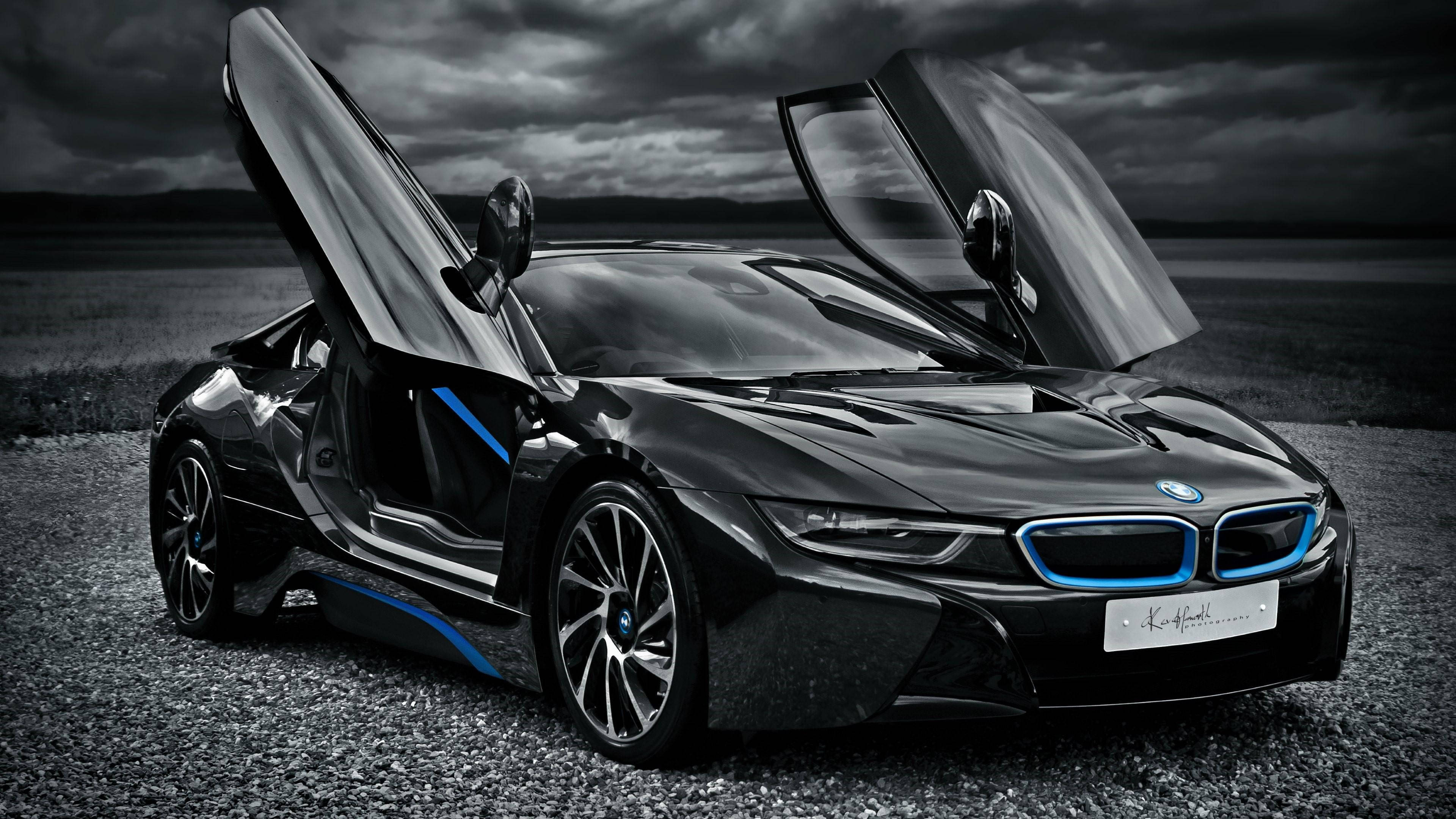 BMW 動圖 桌布 壁紙 — 一輛時尚的黑色BMW i8跑車，鷗翼車門打開，停在碎石上，背景是暴風雨天空，帶有藍色發光點綴。