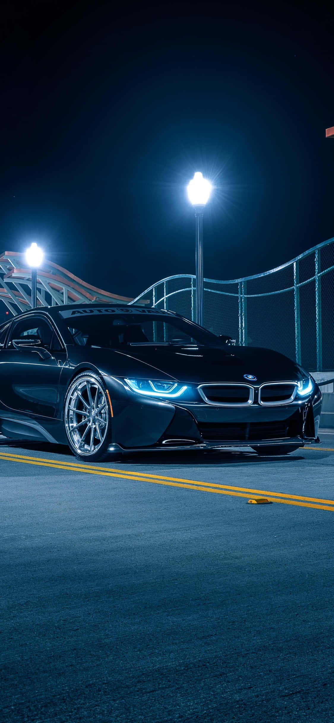 iPhone X Bmw 桌布 壁紙 — 一輛時尚的黑色BMW i8跑車在夜間明亮的體育場燈光下，在黑暗的瀝青賽道上閃閃發光。