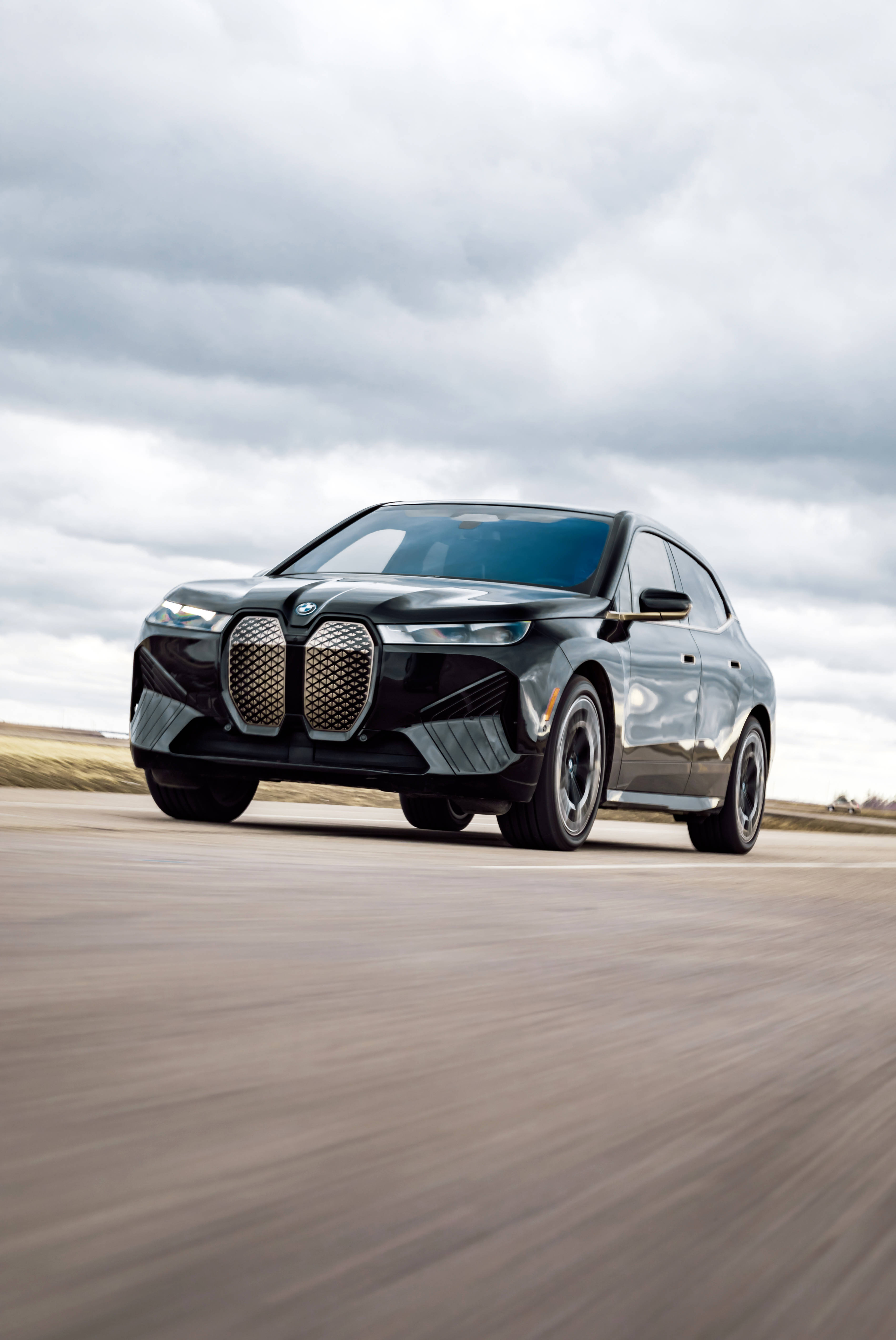 m 桌布 壁紙 — 一輛時尚的黑色BMW iX電動SUV在陰天下一條模糊的沙漠公路上疾馳。