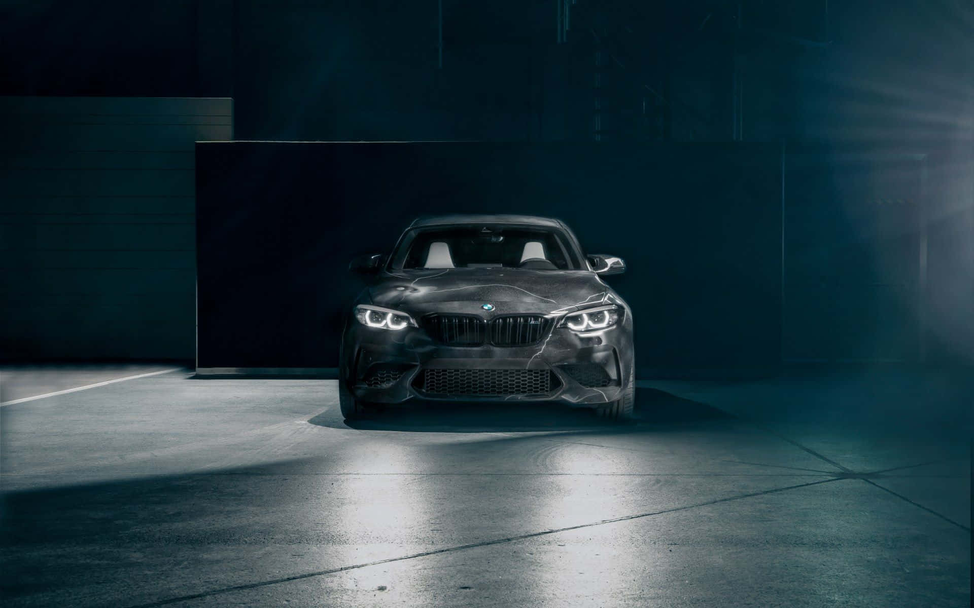 Cool Bmw 桌布 壁紙 — 一輛時尚的黑色BMW M2跑車在昏暗的工業車庫中，於戲劇性的聚光燈下閃耀，氣氛迷濛。