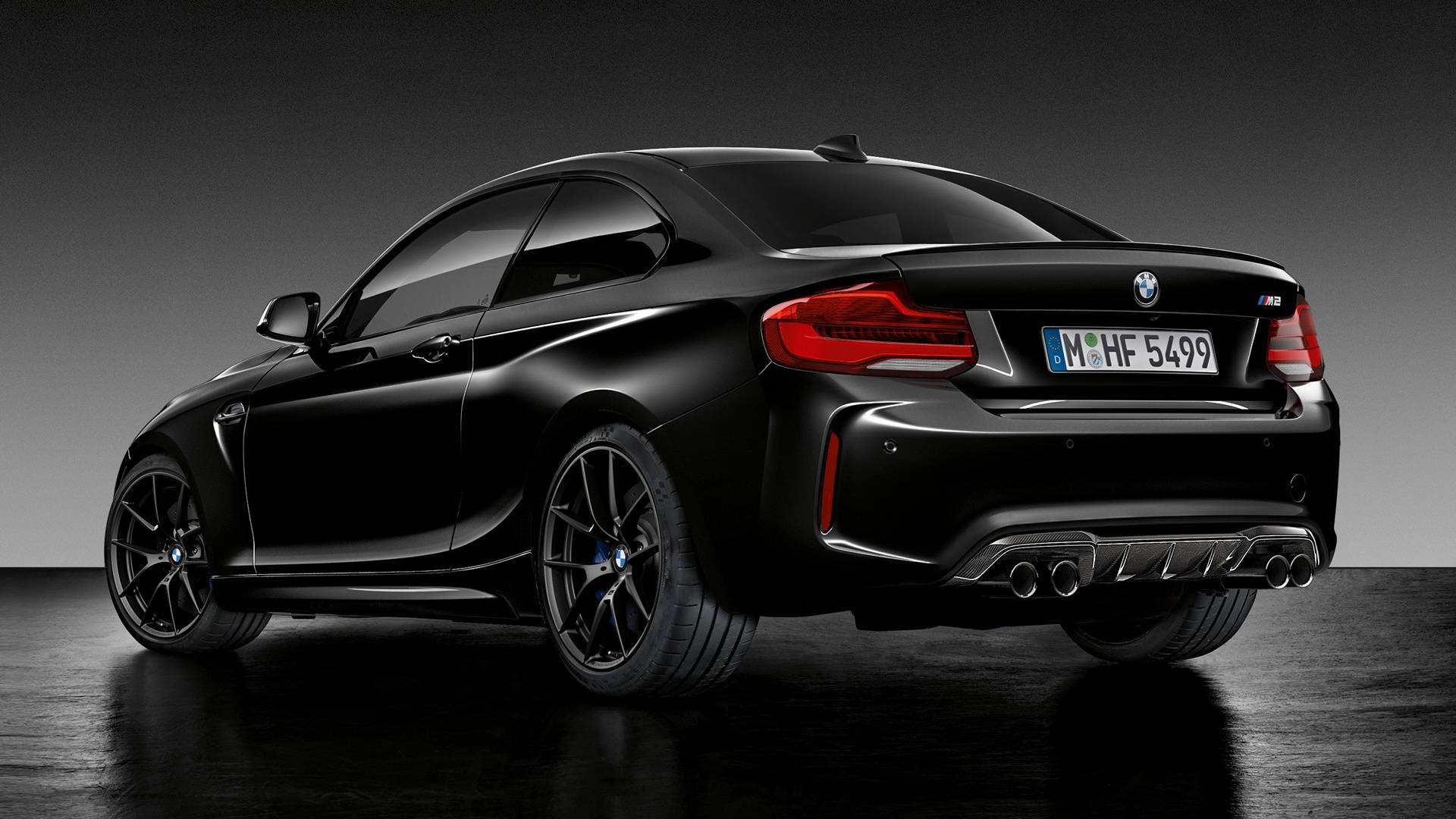 Black Bmw 桌布 壁紙 — 一輛時尚的黑色BMW M2雙門轎跑車，從後方四分之三角度展示，帶有發光的紅色尾燈和四出排氣管，位於深色工作室地板上。