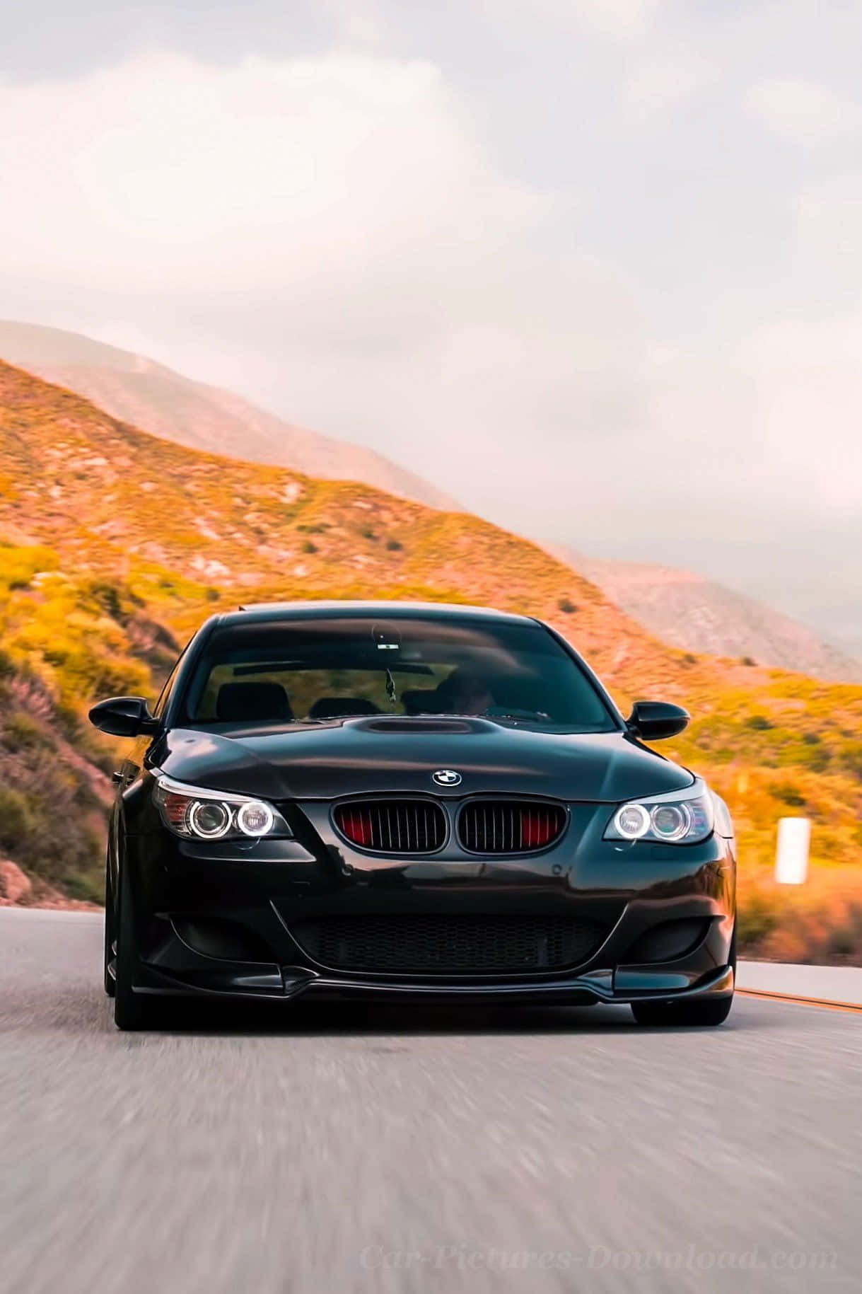 桌布 壁紙 — 一輛時尚的黑色BMW M3在蜿蜒的山路上疾馳，沐浴在金色的夕陽光芒中。