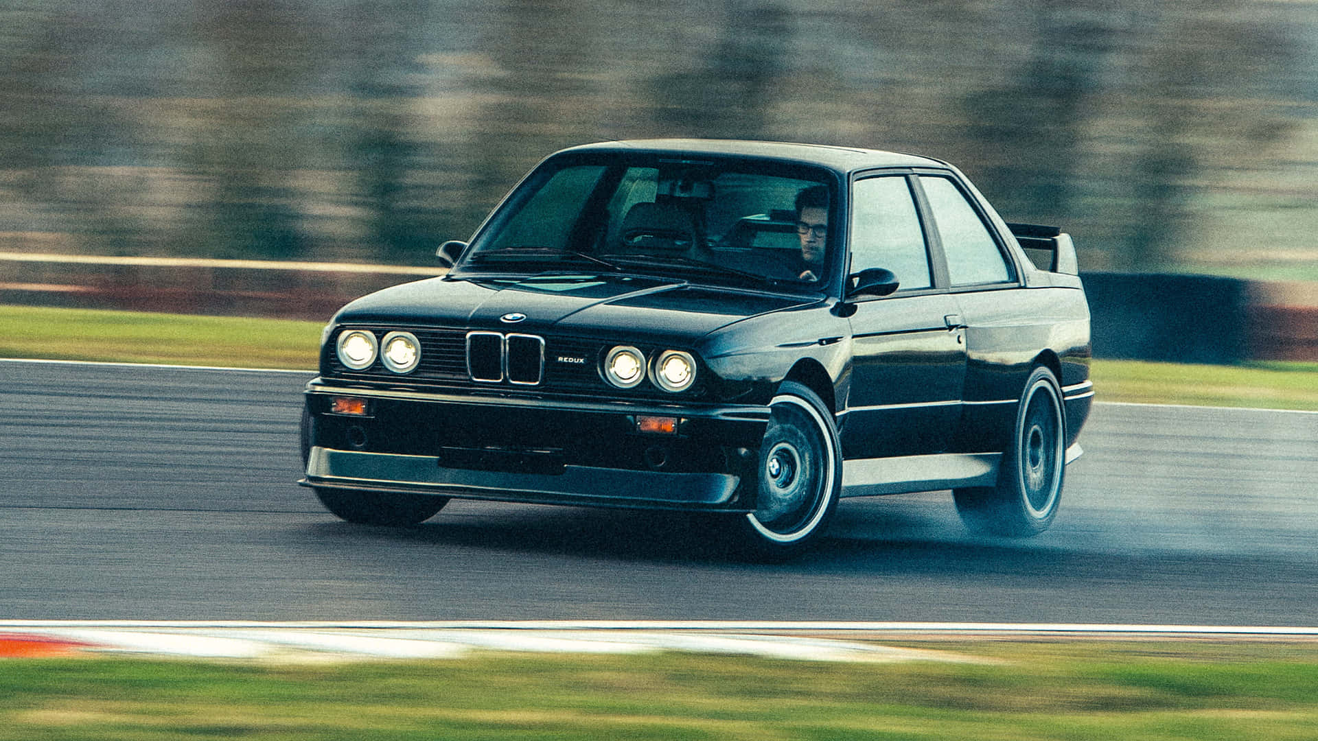 BMW 動圖 桌布 壁紙 — 一輛時尚的黑色BMW M3在賽道上奔馳，動態模糊效果傳達高速與精準。